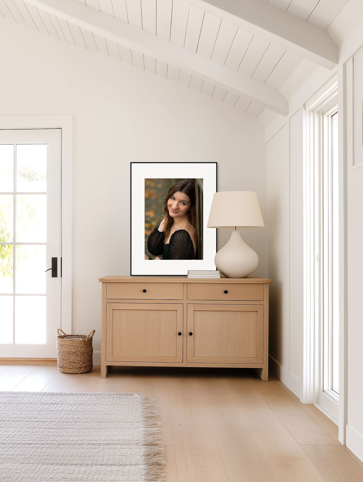 Framed senior portrait of a smiling young woman with long dark hair displayed above a wooden cabinet in a bright room.