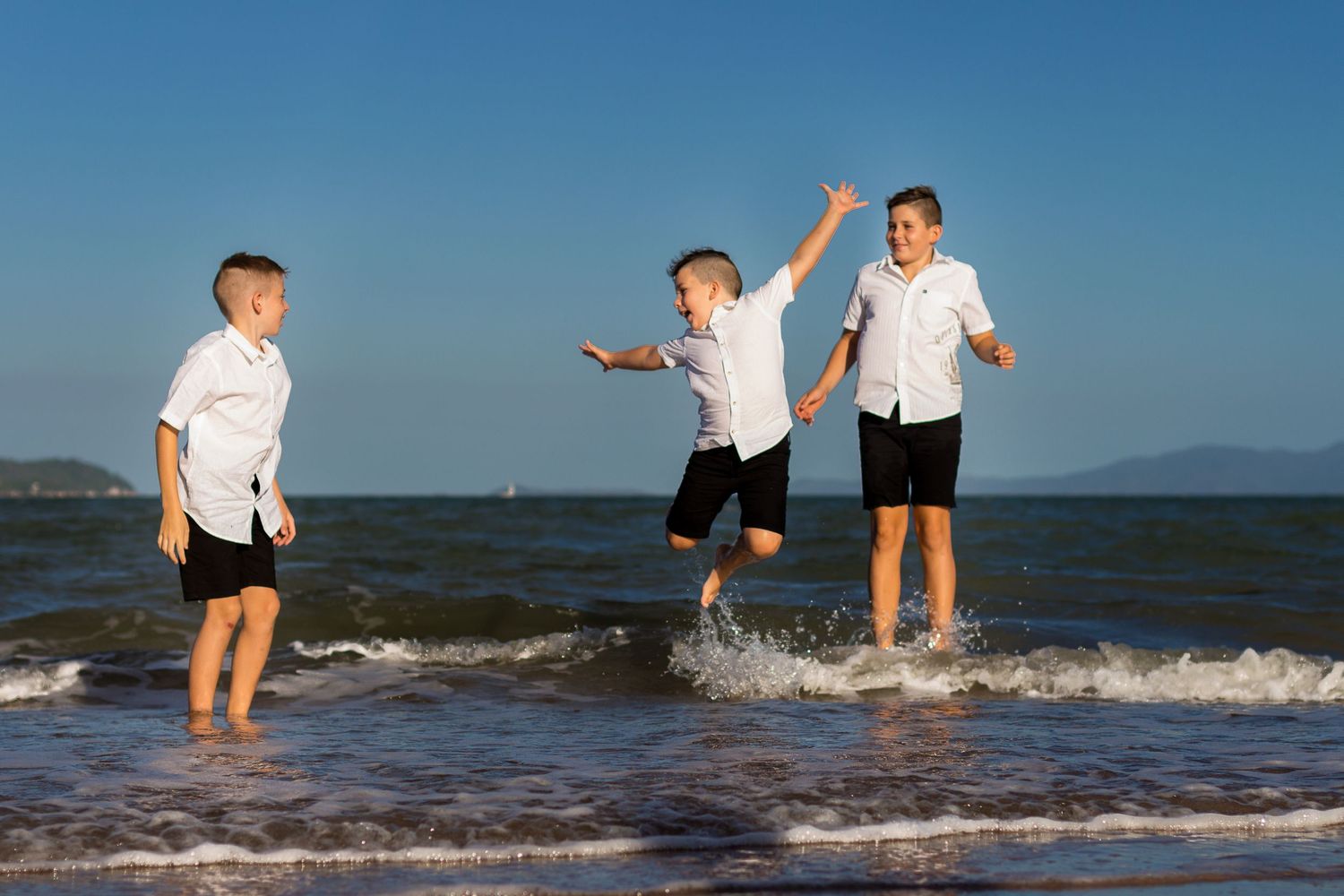 Three children playing together in shallow ocean water at the beach.
