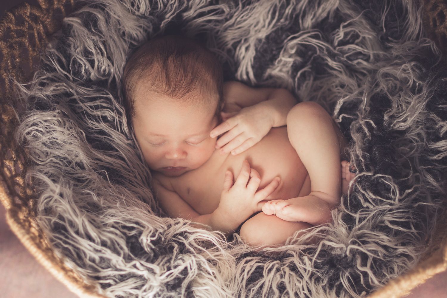 Sleeping newborn baby curled uo on a dark fluffy blanket.