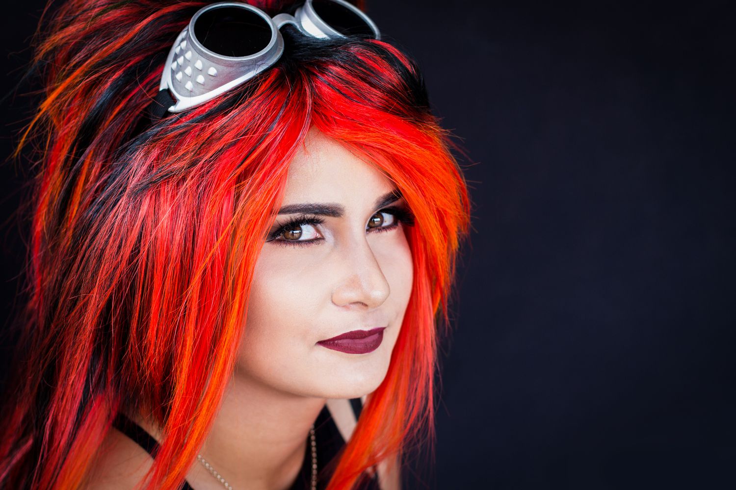 Portrait of a red-haired woman wearing goggles on her head.
