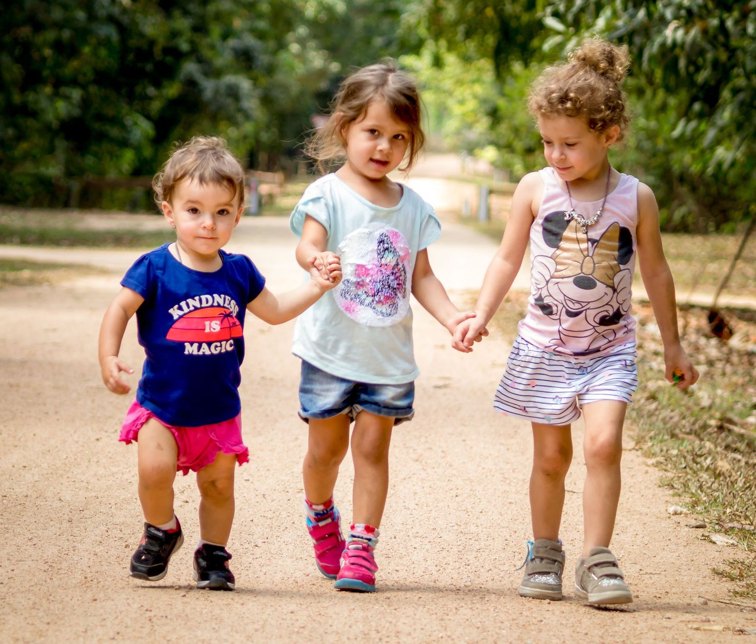 Three young children walking hand in hand together outdoors.