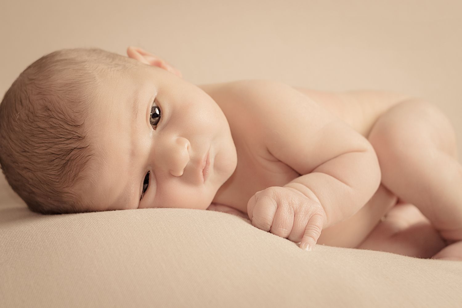 Newborn baby lying awake on a soft cream blanket during a newborn photography session.