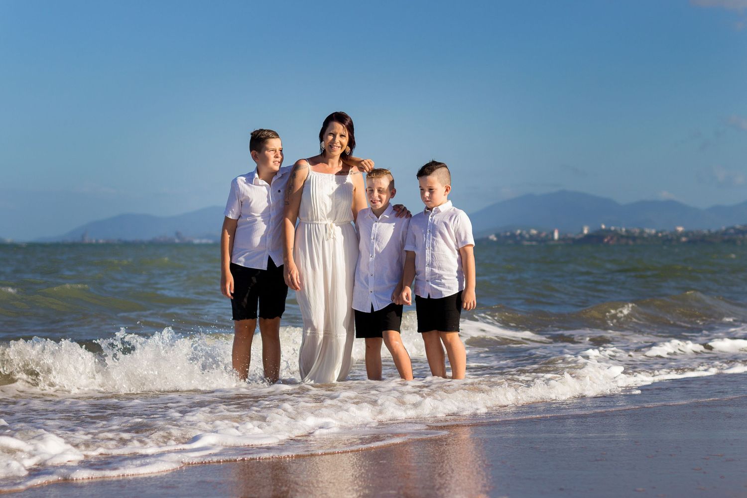 Family standing together in shallow ocean water during a beach photography session.