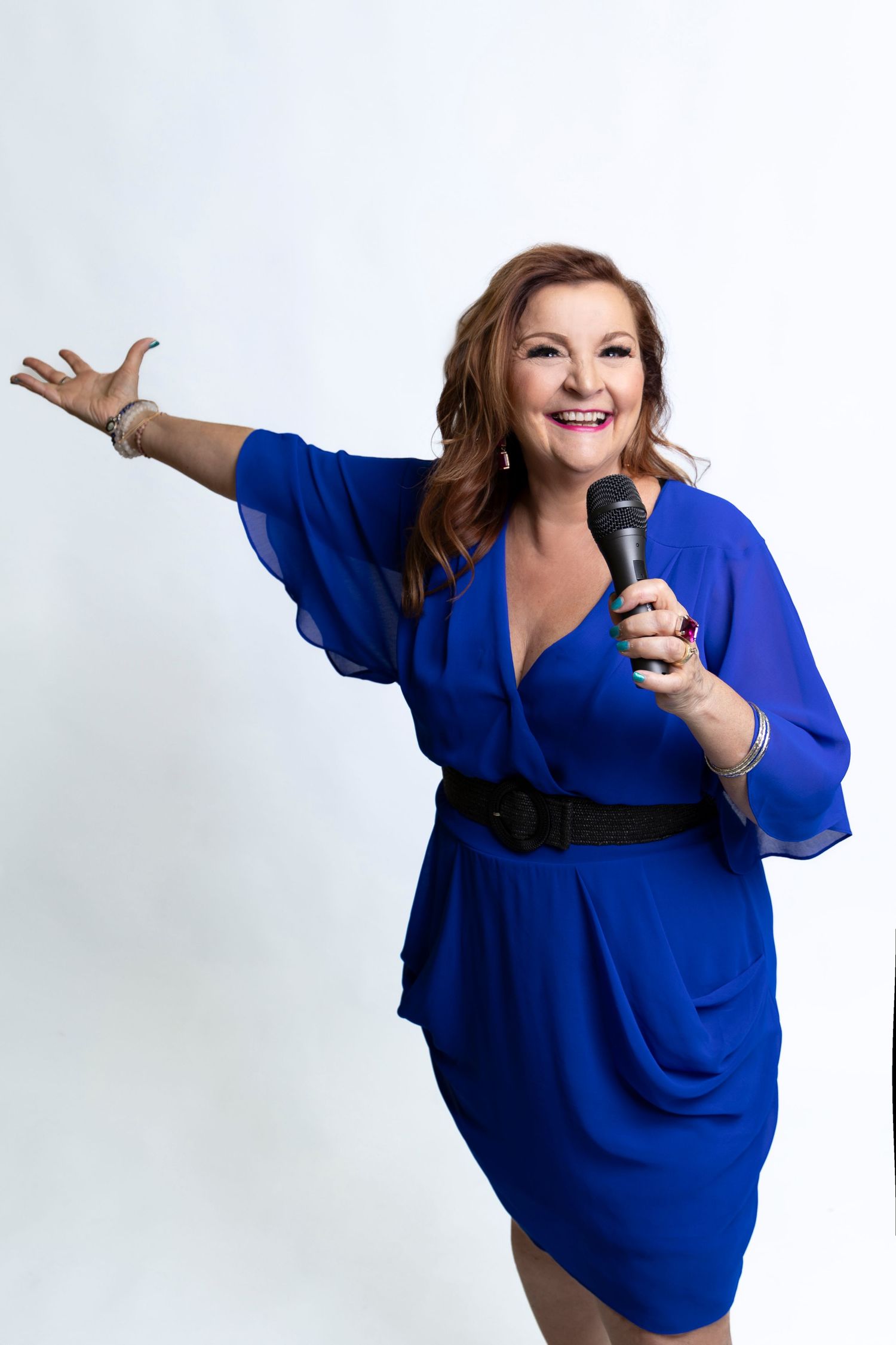 Energetic woman in blue dress holding microphone with arm outstretched on white background.