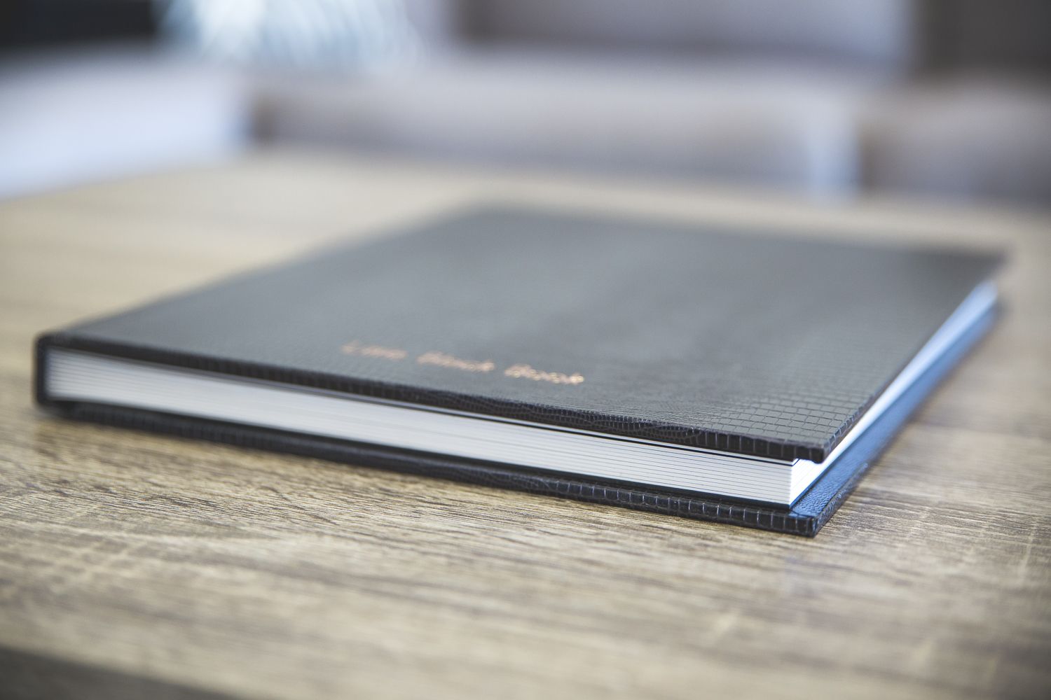 A sleek black leather hardcover book resting on a wooden table with a blurred background.