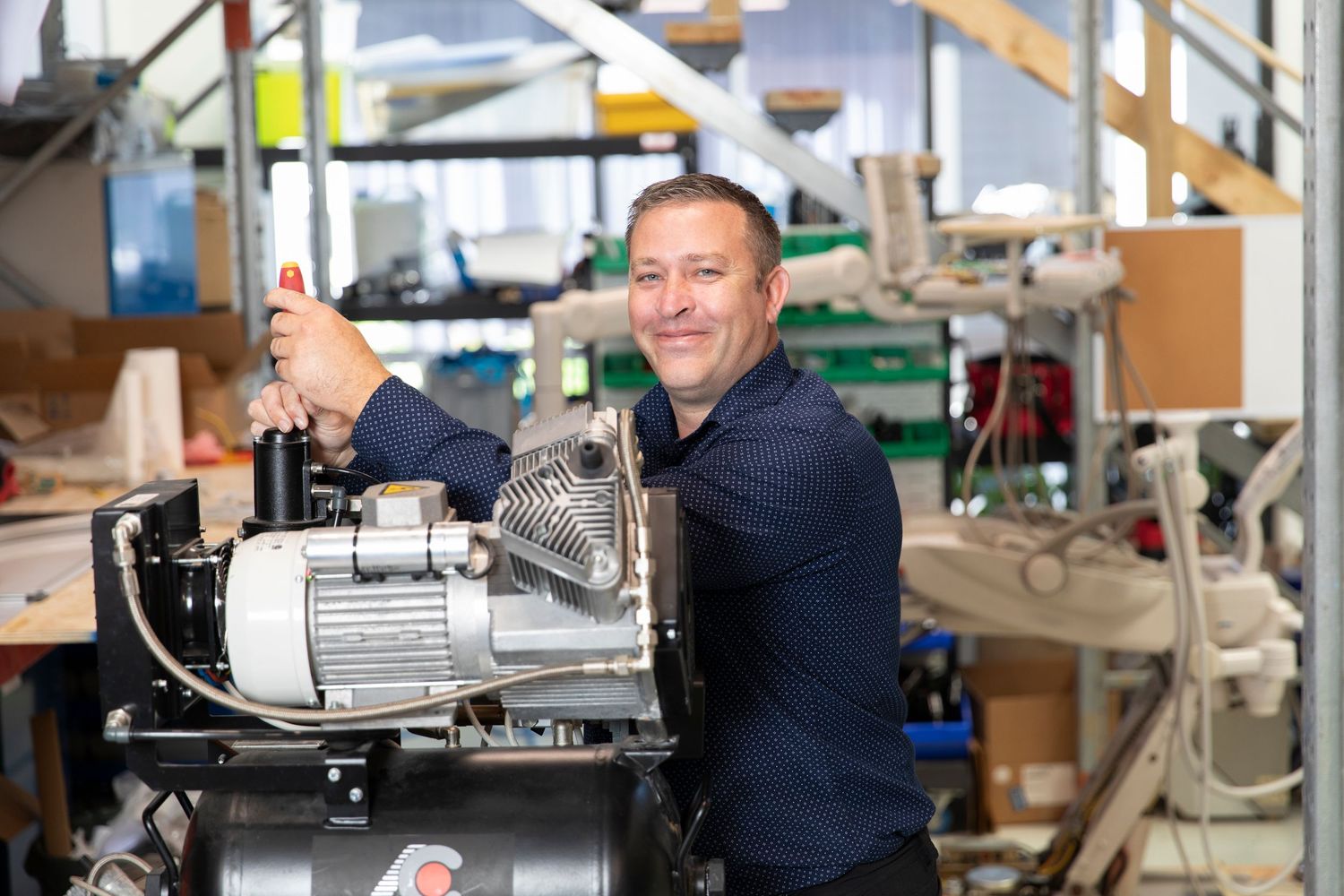 Smiling man working on industrial machinery in a professional workshop environment.