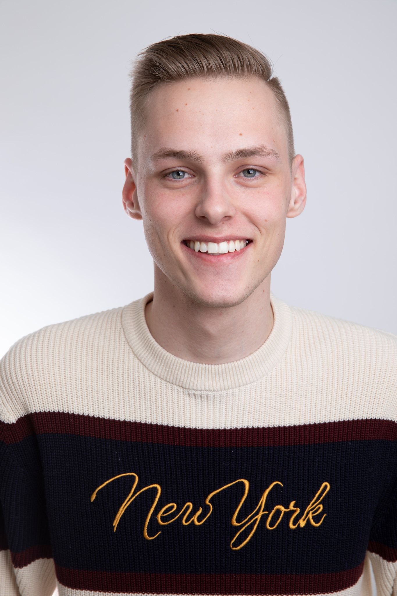 Smiling young blond man wearing New York striped sweater against white background.