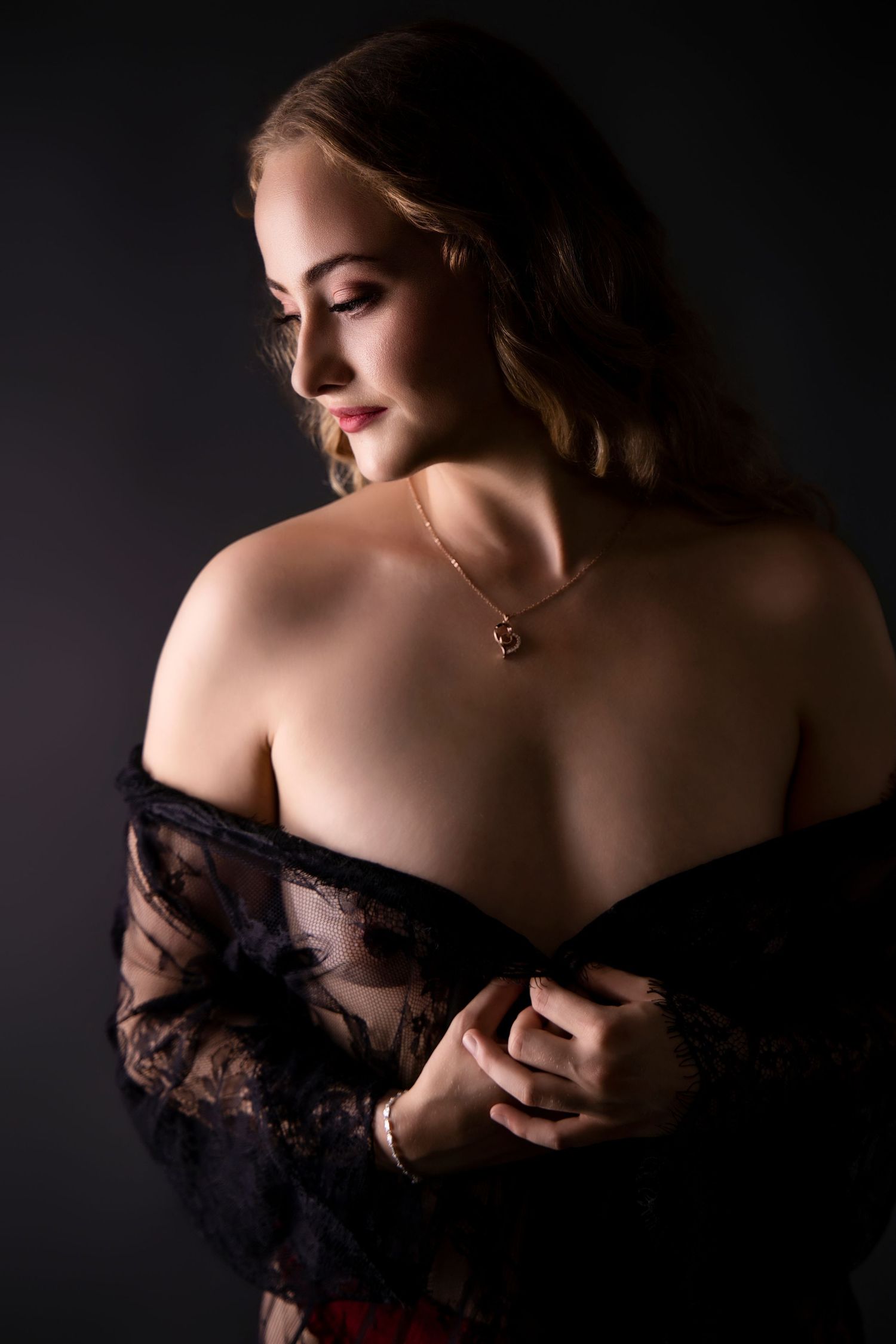 Elegant woman in black lace robe revealing bare back with gold necklace.