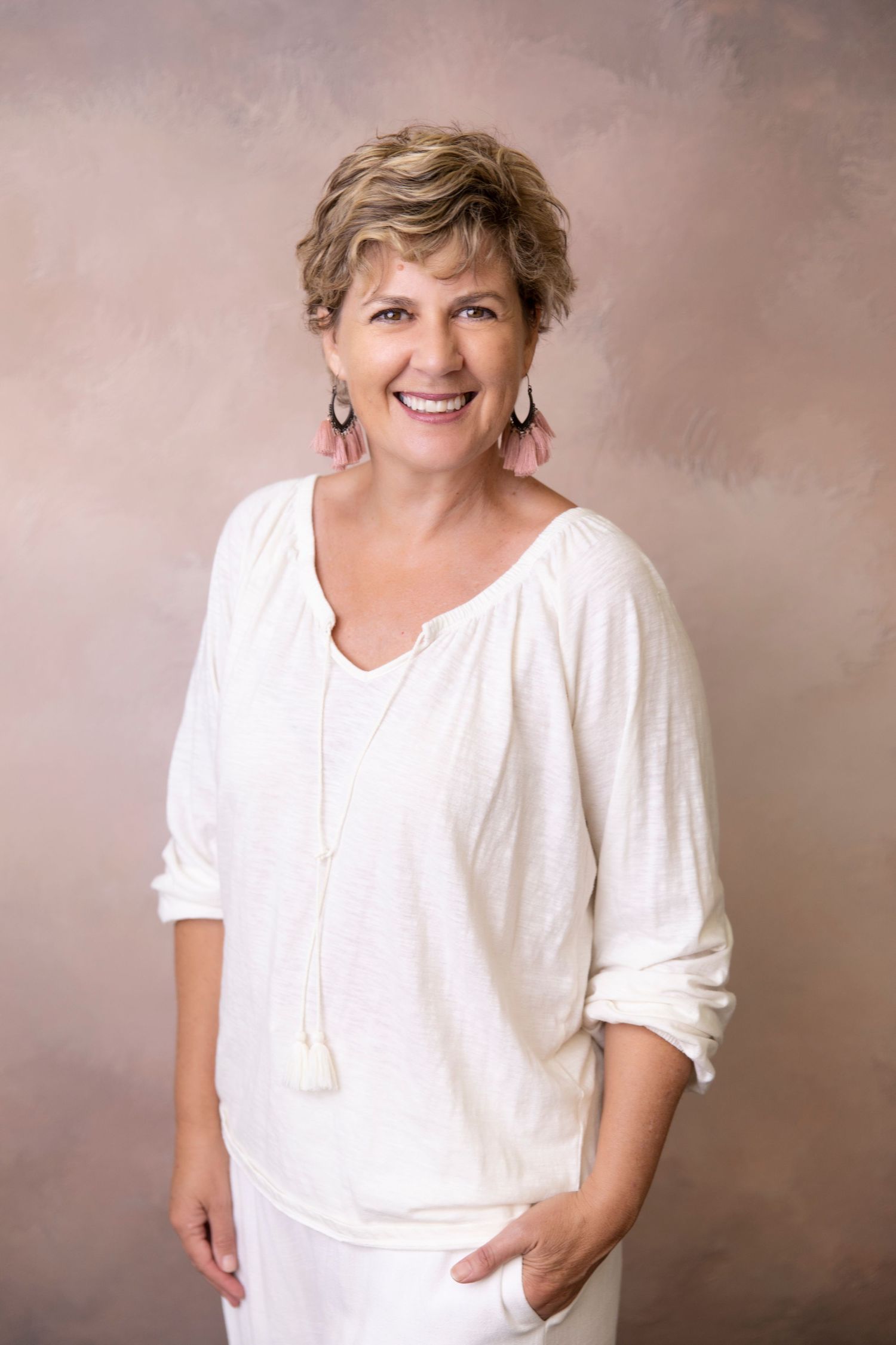 Cheerful woman with short blonde hair in white blouse smiling in a professional portrait studio.