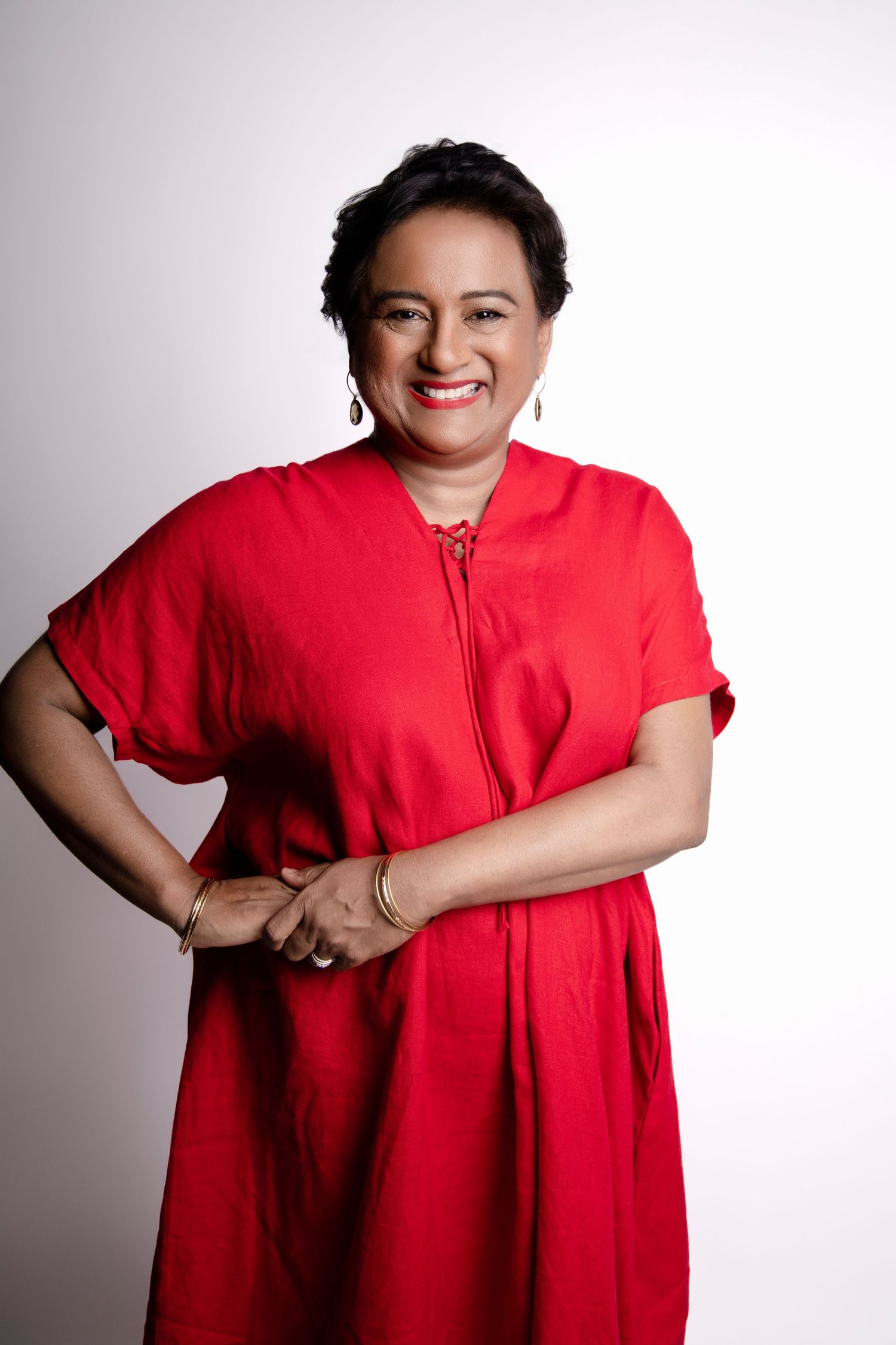 Confident woman in bold red dress smiling with hands clasped against clean white studio background.