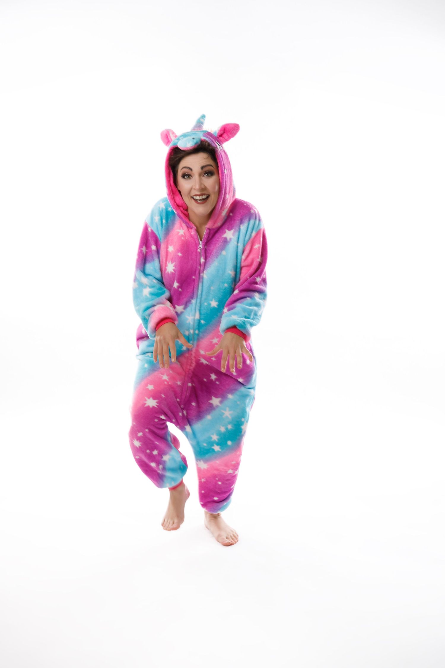 Woman wearing colorful unicorn star print kigurumi onesie pajama on white background.