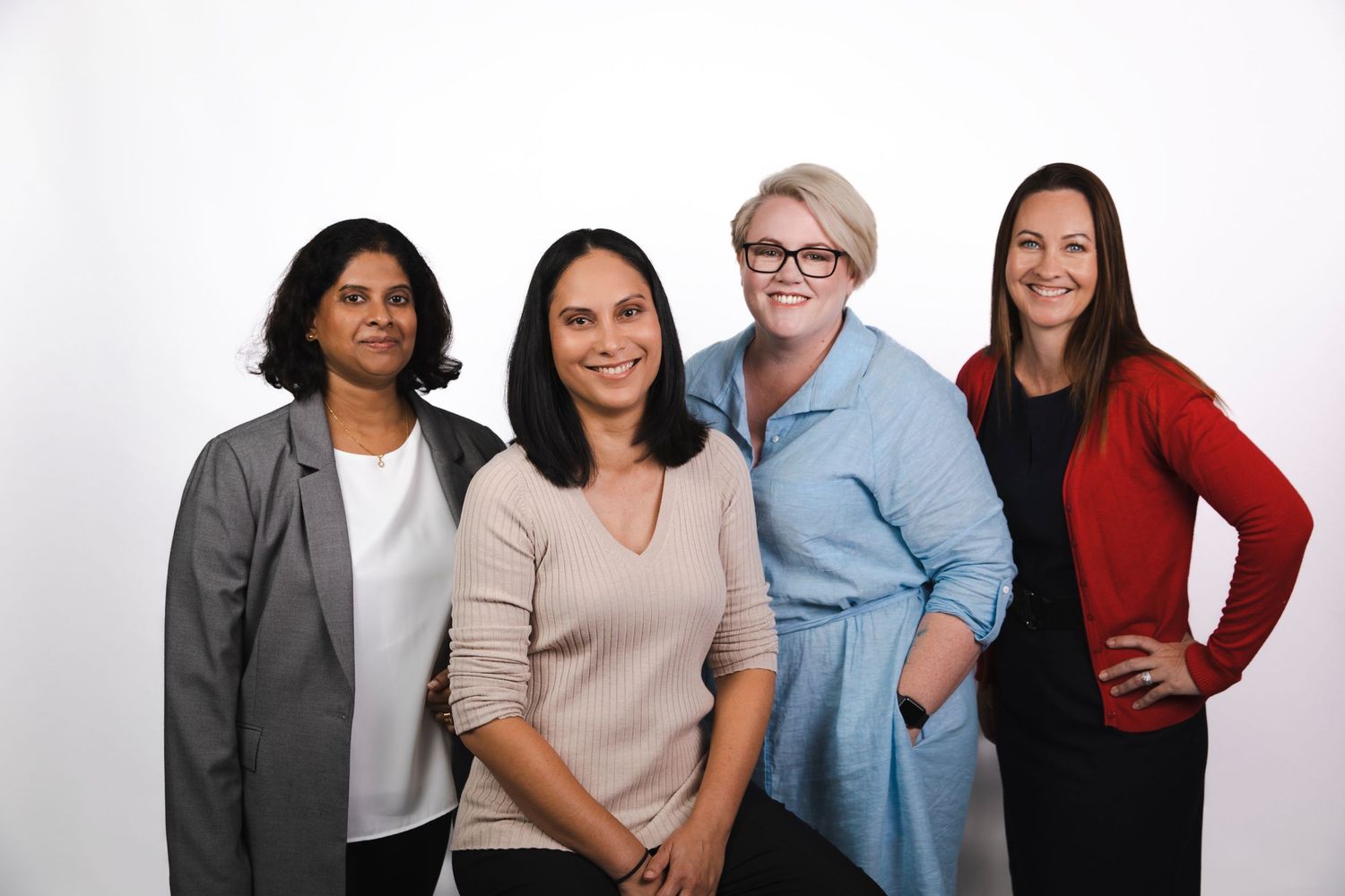 Four professional women smiling together in a group portrait against white background.