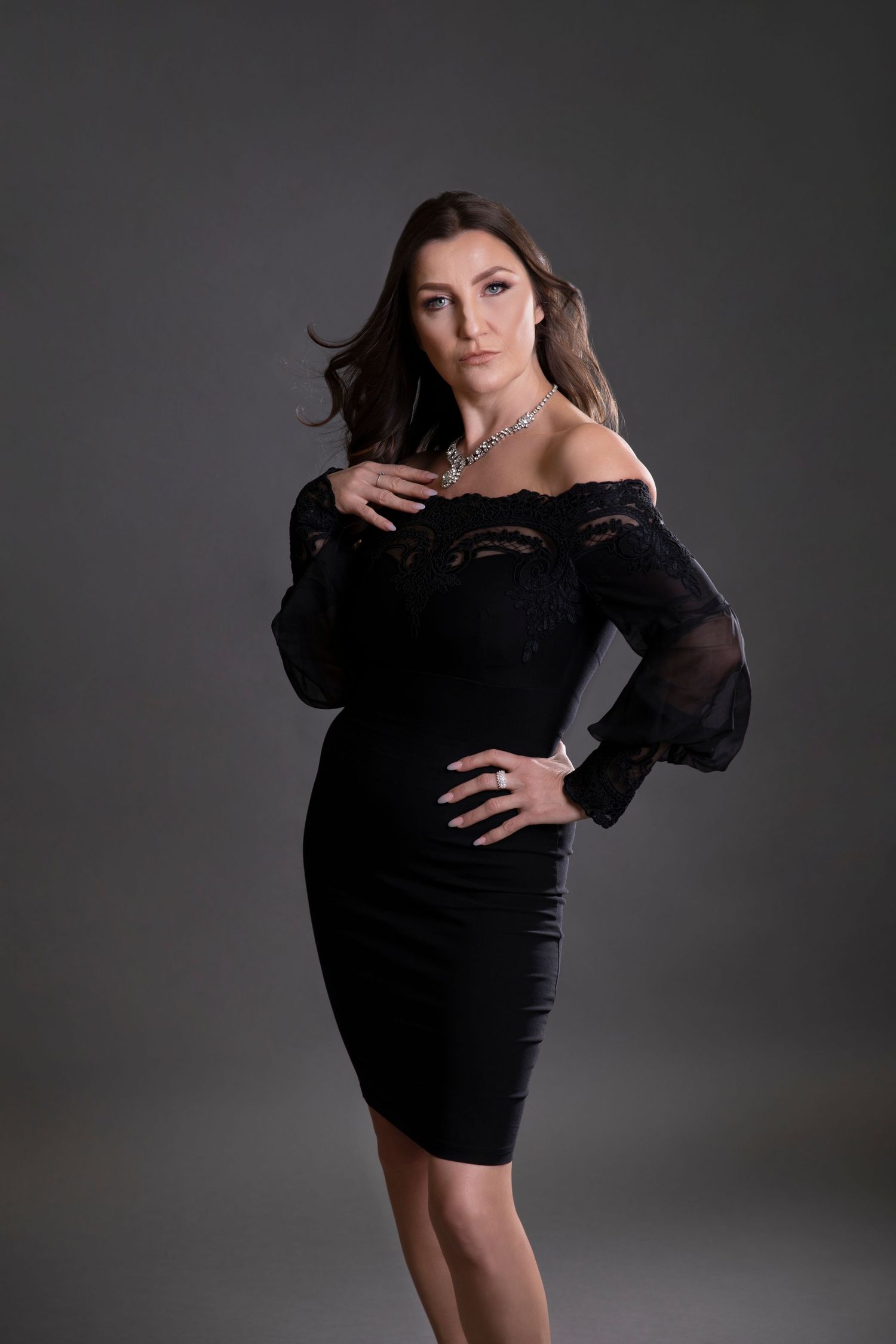 Elegant woman in black off-shoulder lace dress with silver necklace in studio.