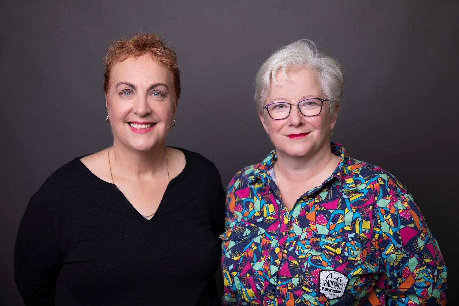 Two smiling women posing together for a professional portrait against dark background.