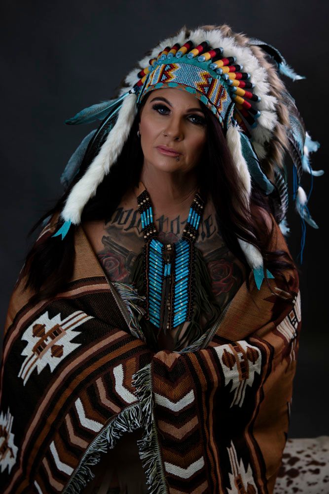 Woman wearing colorful feathered Native American headdress wrapped in tribal blanket.