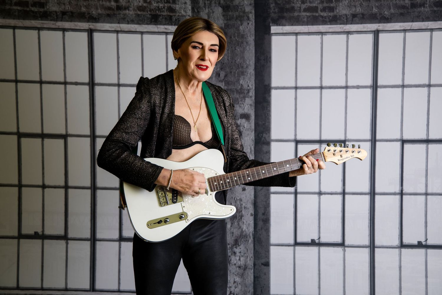 Woman in black leather jacket plays white electric guitar in a studio setting.