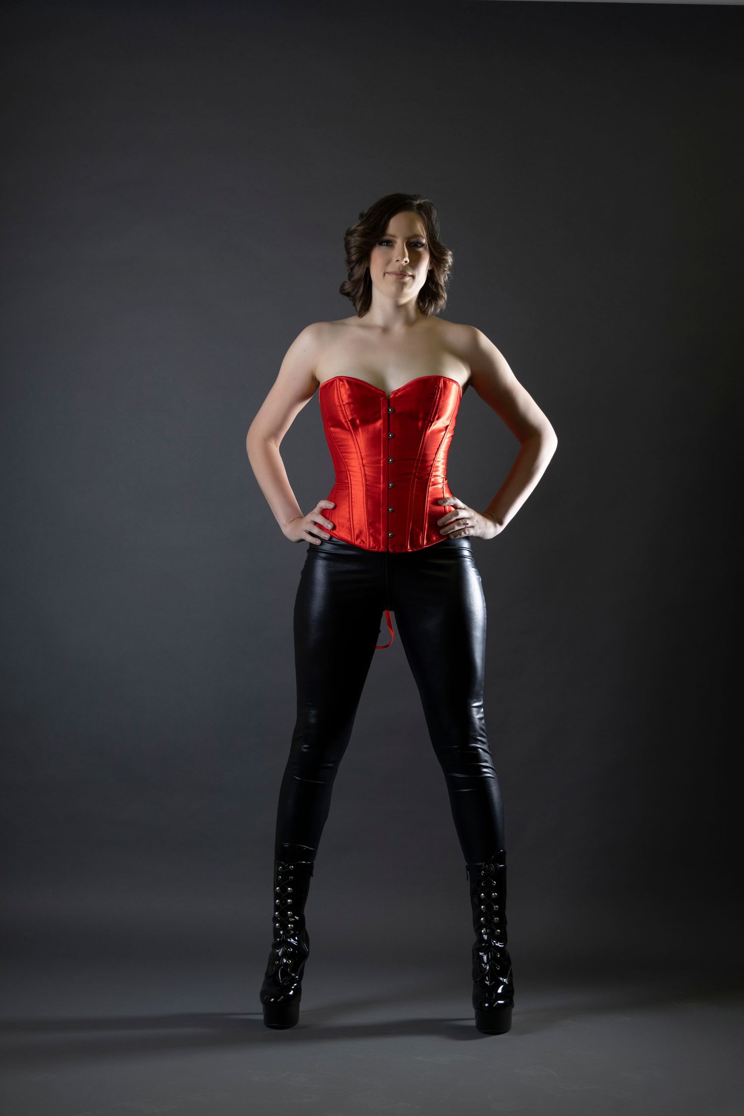 Woman in red corset top and black leather pants with platform boots in studio.