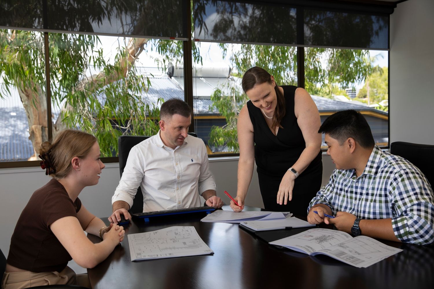 Four colleagues reviewing architectural plans together at conference table in bright office.