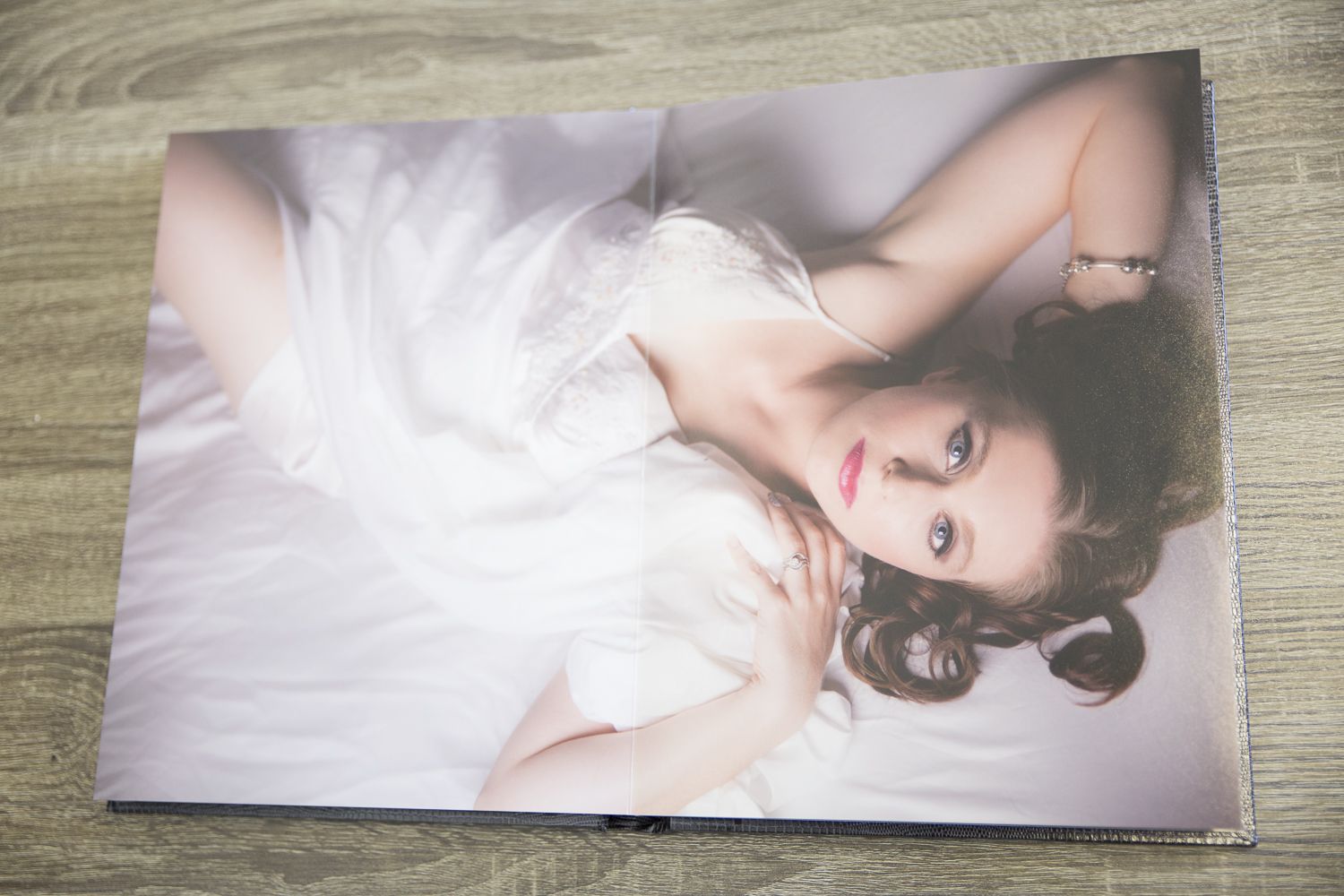 A young woman in a white dress poses elegantly on a bed, featured in a professional portrait photography print.