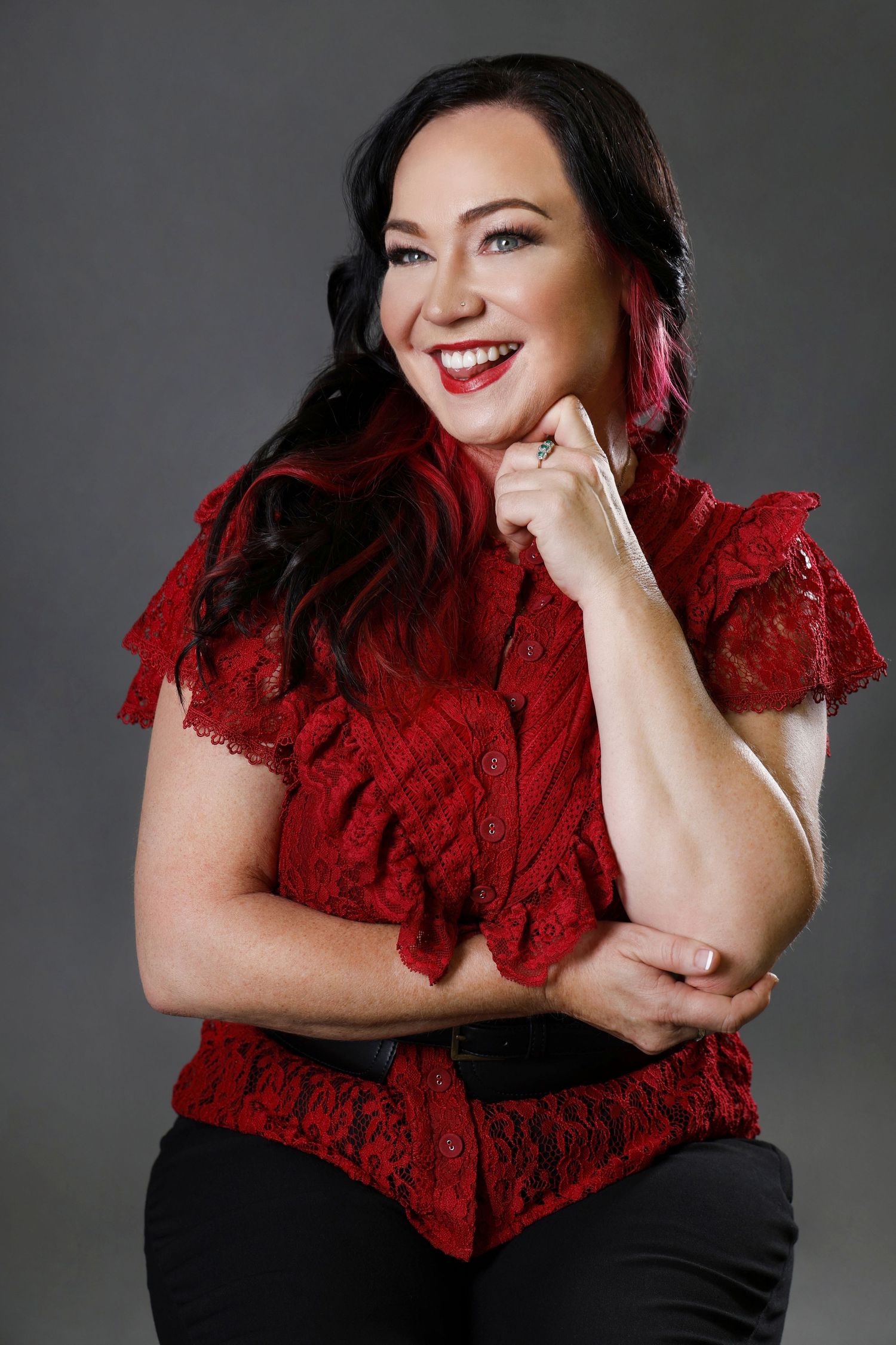 Cheerful woman in red lace blouse smiling in studio portrait on gray background.