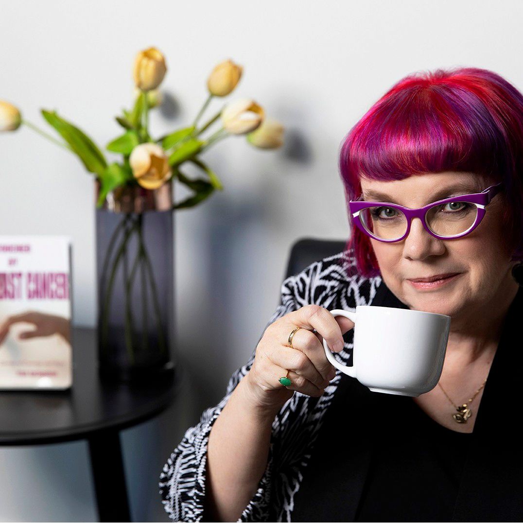 Woman with pink hair and purple glasses holding coffee cup near tulips and book display.