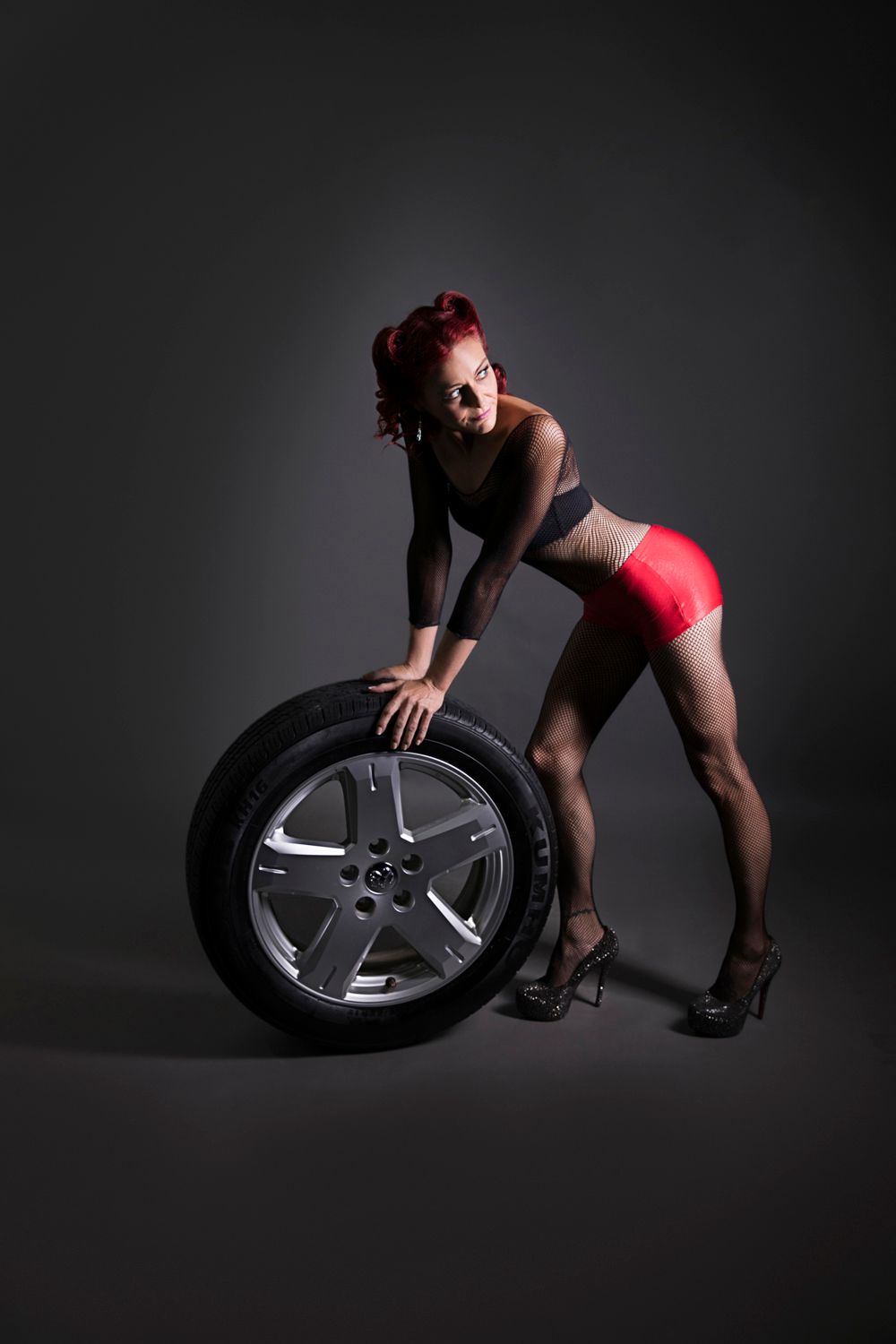 Red-haired pin-up woman in red skirt poses with car tire in studio.