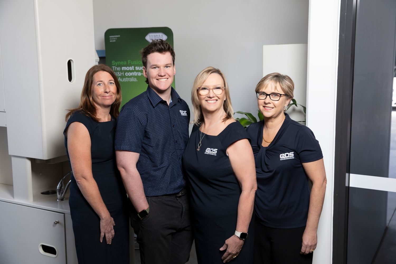 Team of four professionals in matching dark uniforms posing together in a modern office.