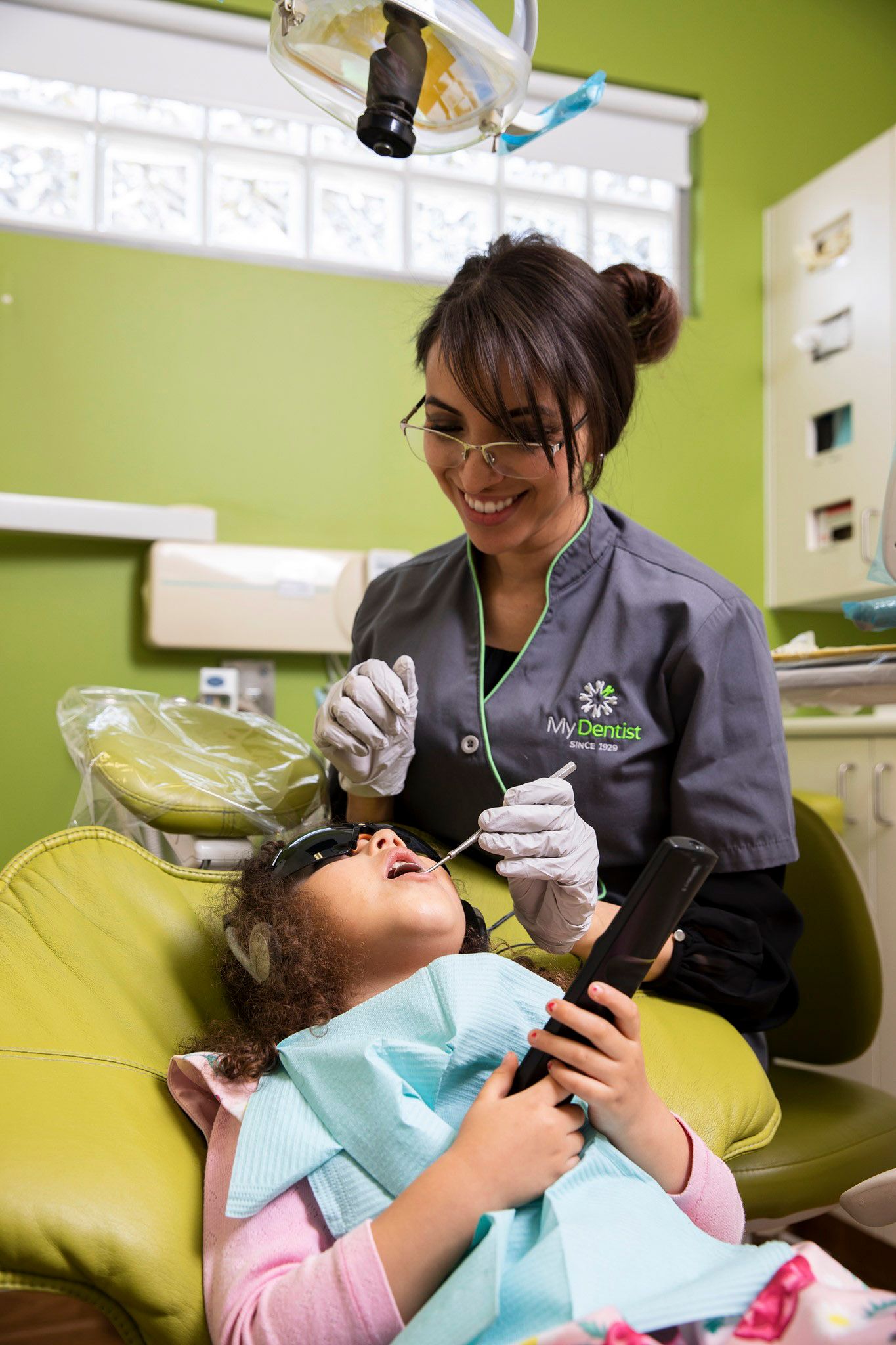 Female dental hygienist treating young child patient in bright green dental office.