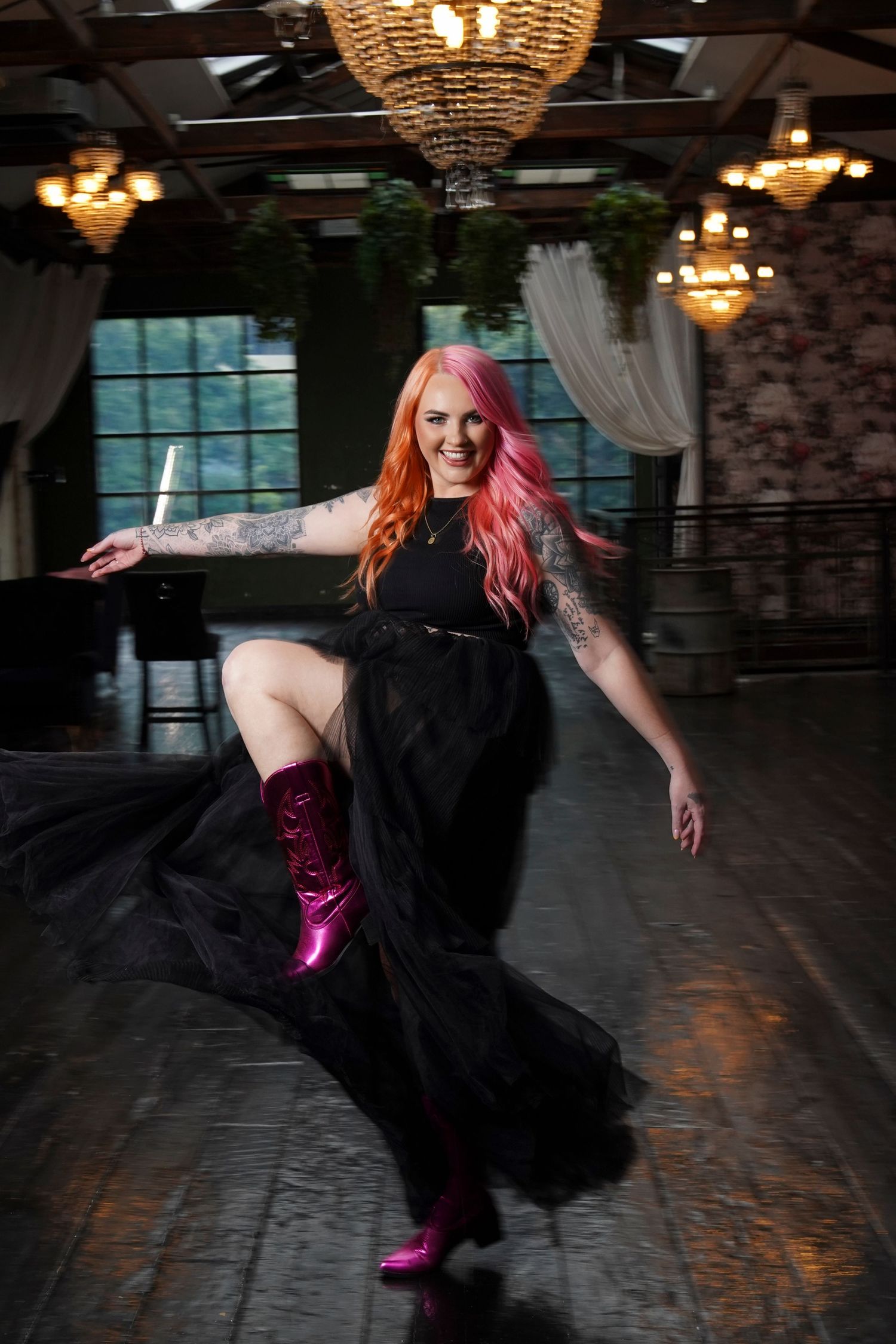 Woman with pink hair in black tulle skirt and pink boots dances in elegant venue.