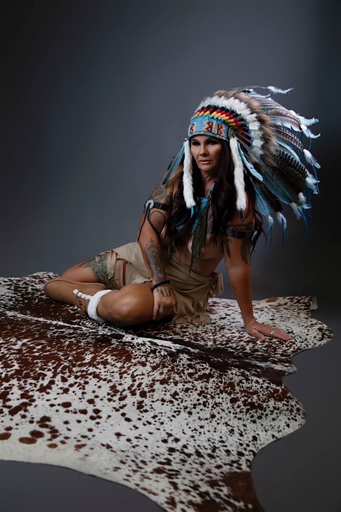 Woman in Native American headdress and costume posing on animal hide rug.