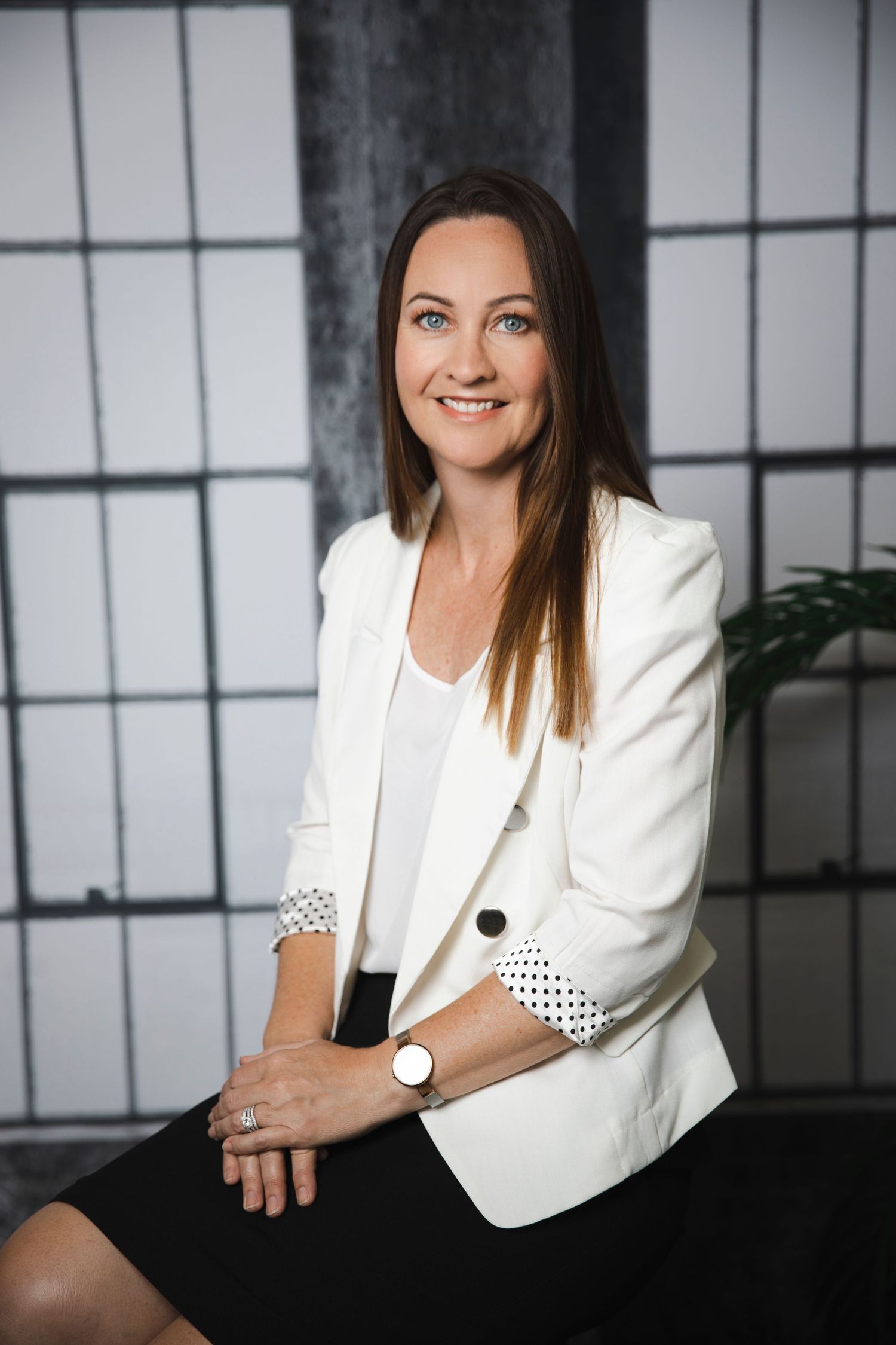 Professional woman in white blazer smiling confidently in a modern studio setting.