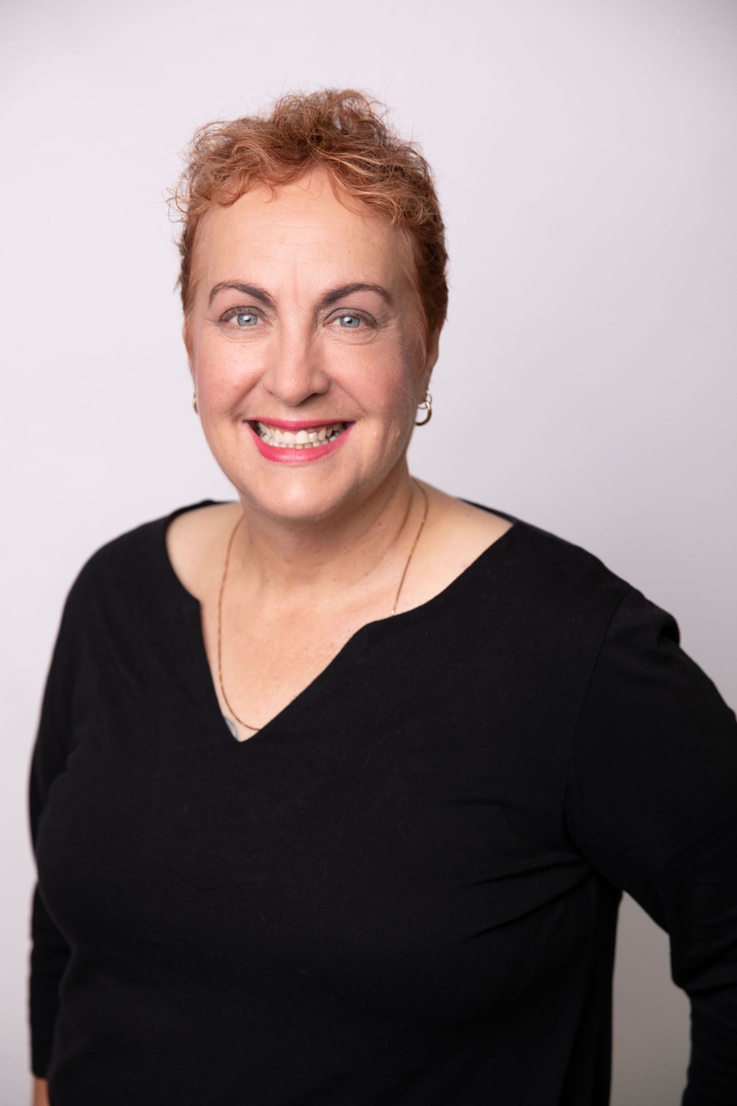 Smiling woman with short red hair in black top posing for professional headshot.