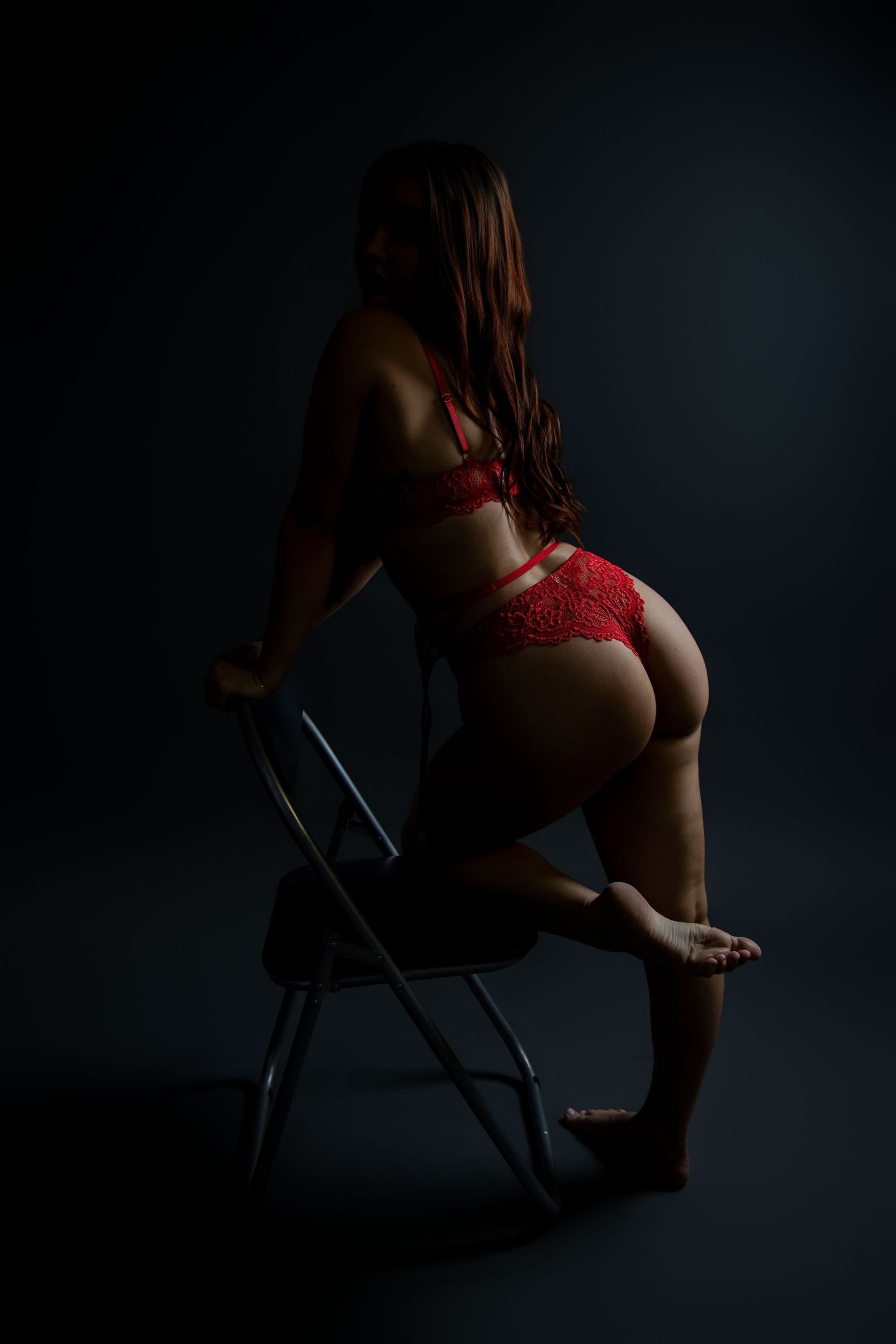 Woman in red lace lingerie posing on a chair in dramatic dark studio lighting.