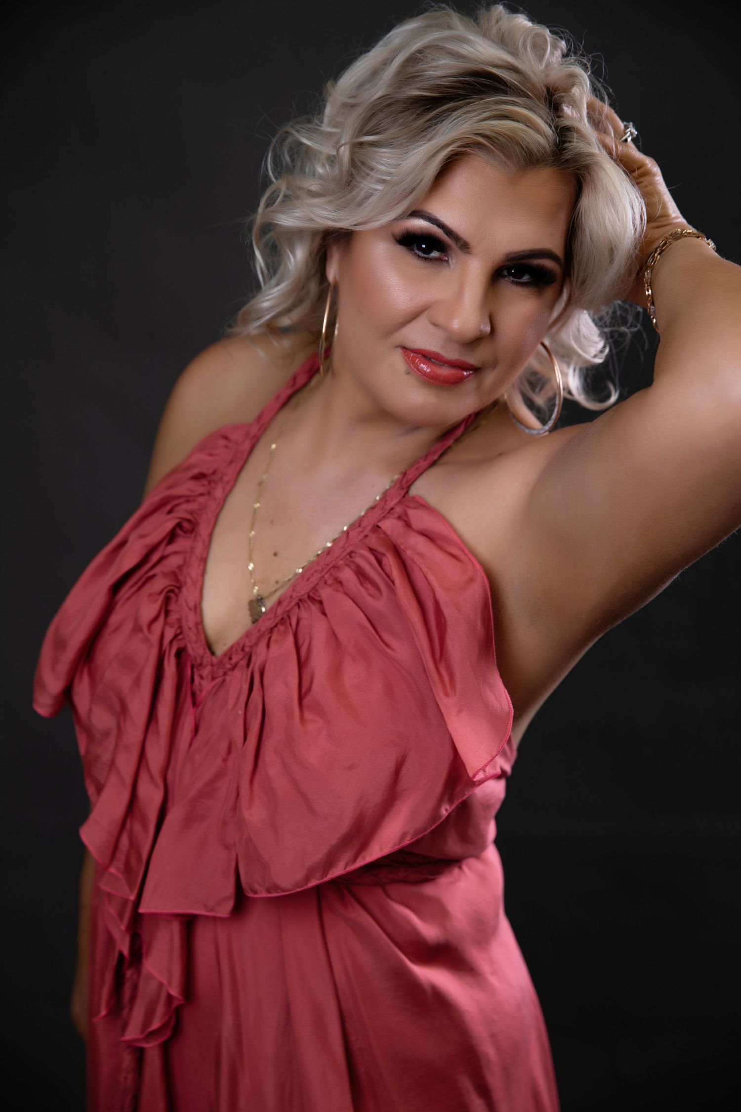 Blonde woman in pink satin halter dress posing confidently against dark gray studio background.