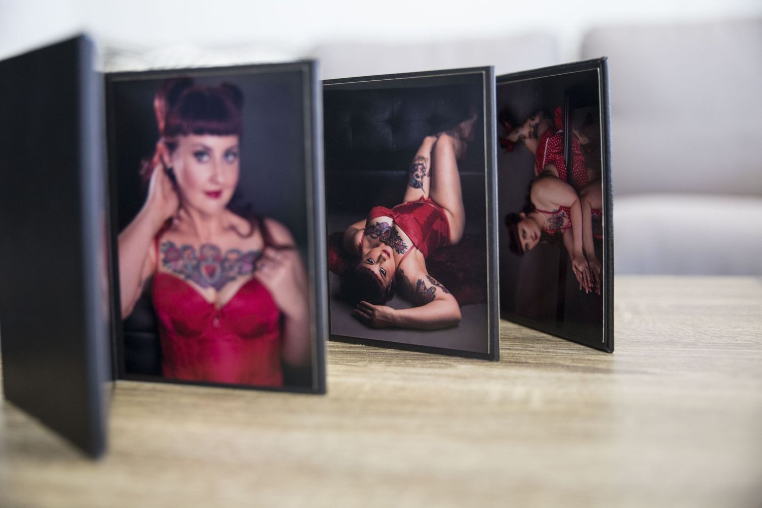 Three framed boudoir photos of a tattooed woman in red lingerie displayed on a wooden surface.