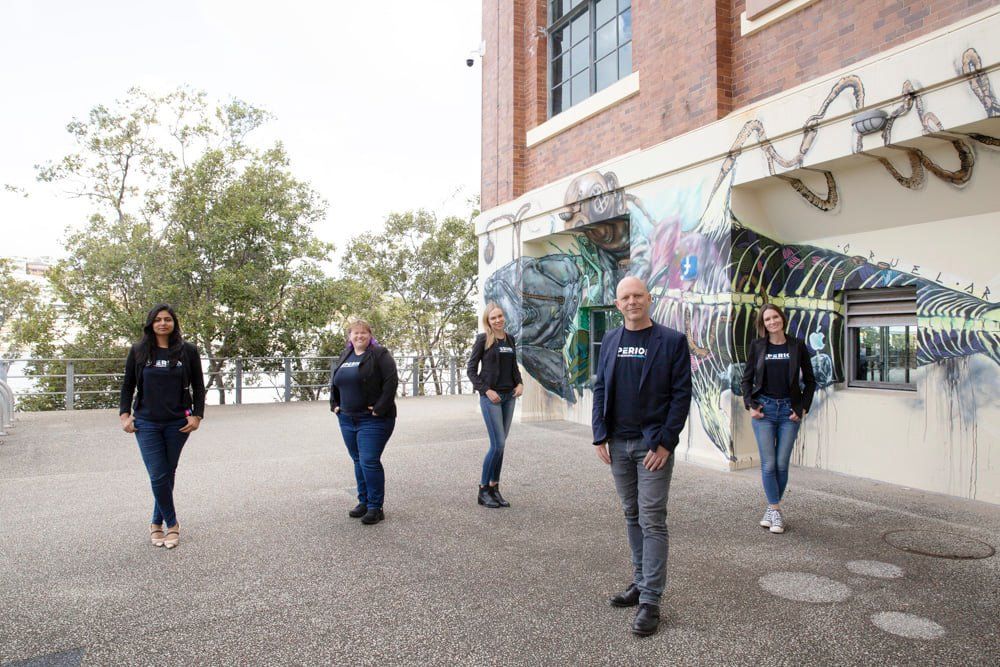 Group of five professionals standing outdoors near colorful mural on brick building wall.