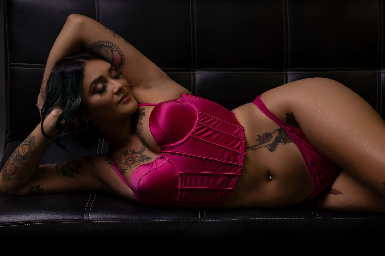 Woman with tattoos in pink bikini set posing on black leather couch.