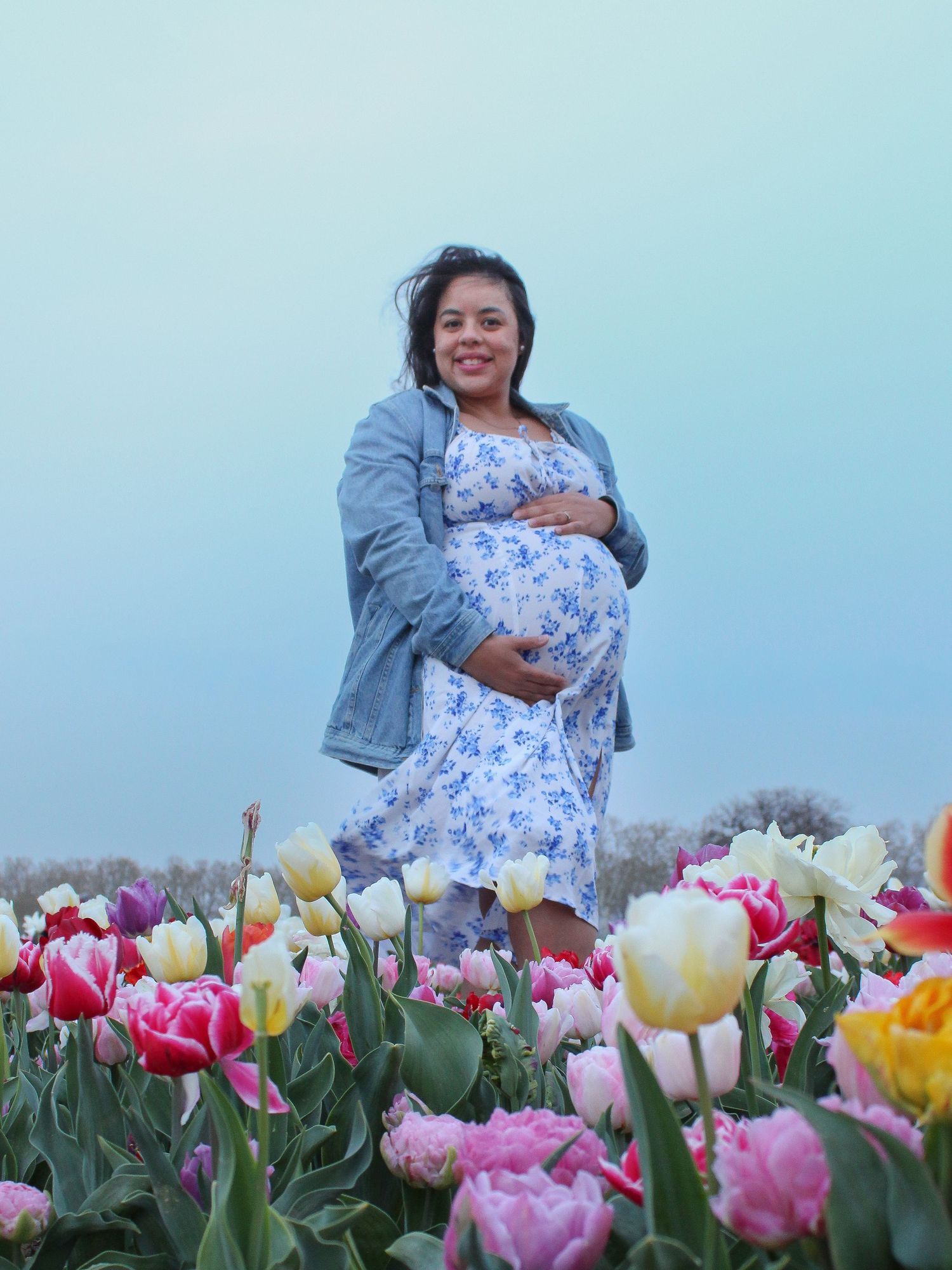 Une future maman pose en extérieur en tenant son ventre pendant une séance photo grossesse dans un champs de tulips