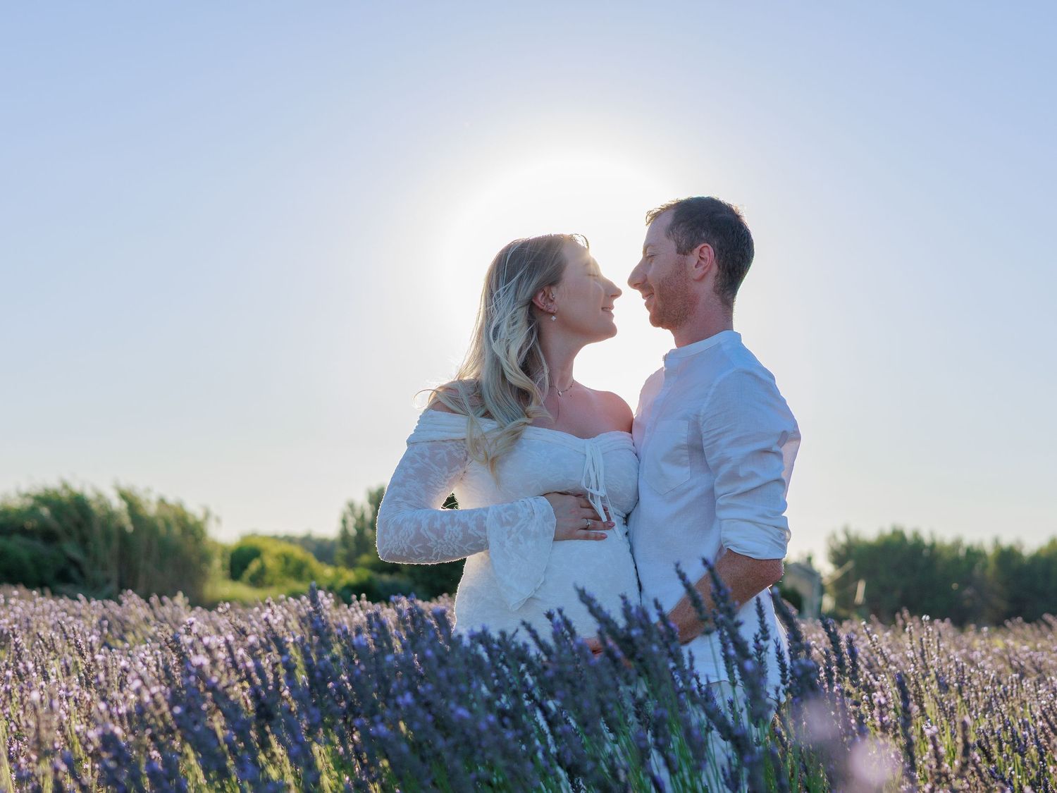 Un couple de futurs parents s’embrasse dans un champ de lavande pres d'Orange pendant une séance photo grossesse.