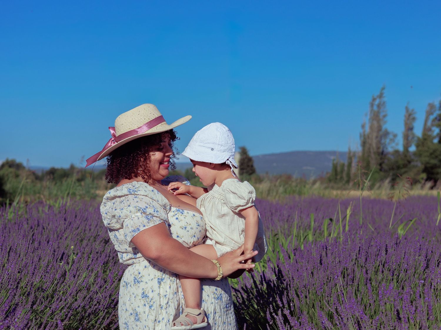 Une maman porte son enfant dans un champ de lavande pendant une séance photo famille en extérieur.