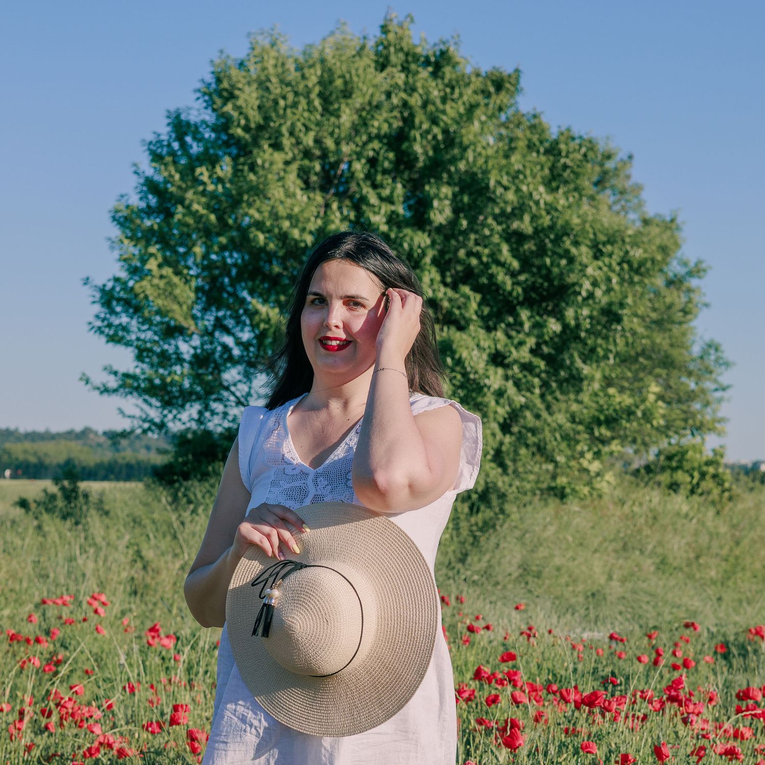 Une femme pose avec un chapeau dans un champ de coquelicots pendant une séance photo portrait en extérieur.