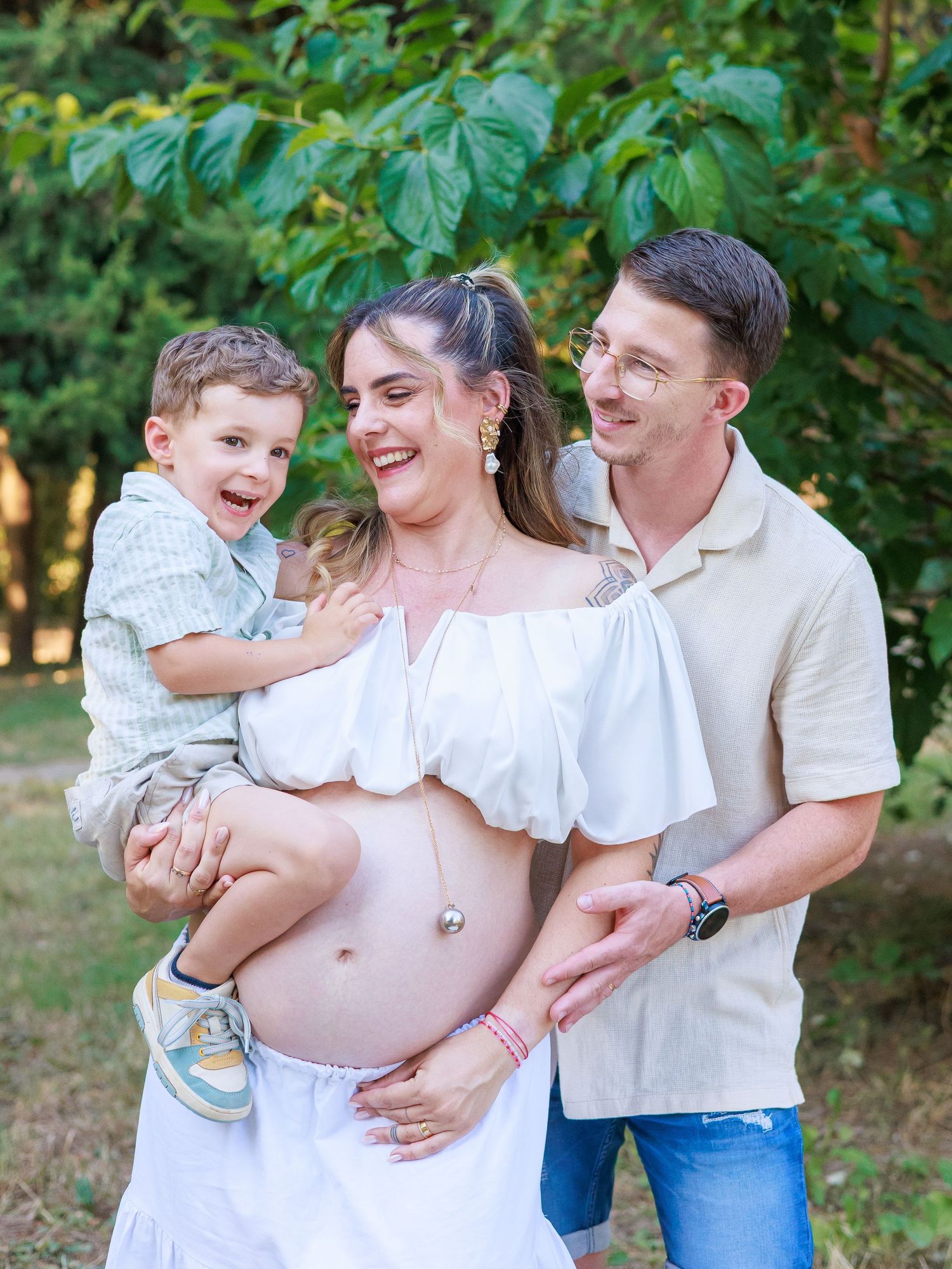 Une famille pose ensemble pendant une séance photo grossesse en extérieur, avec les parents et leur enfant.