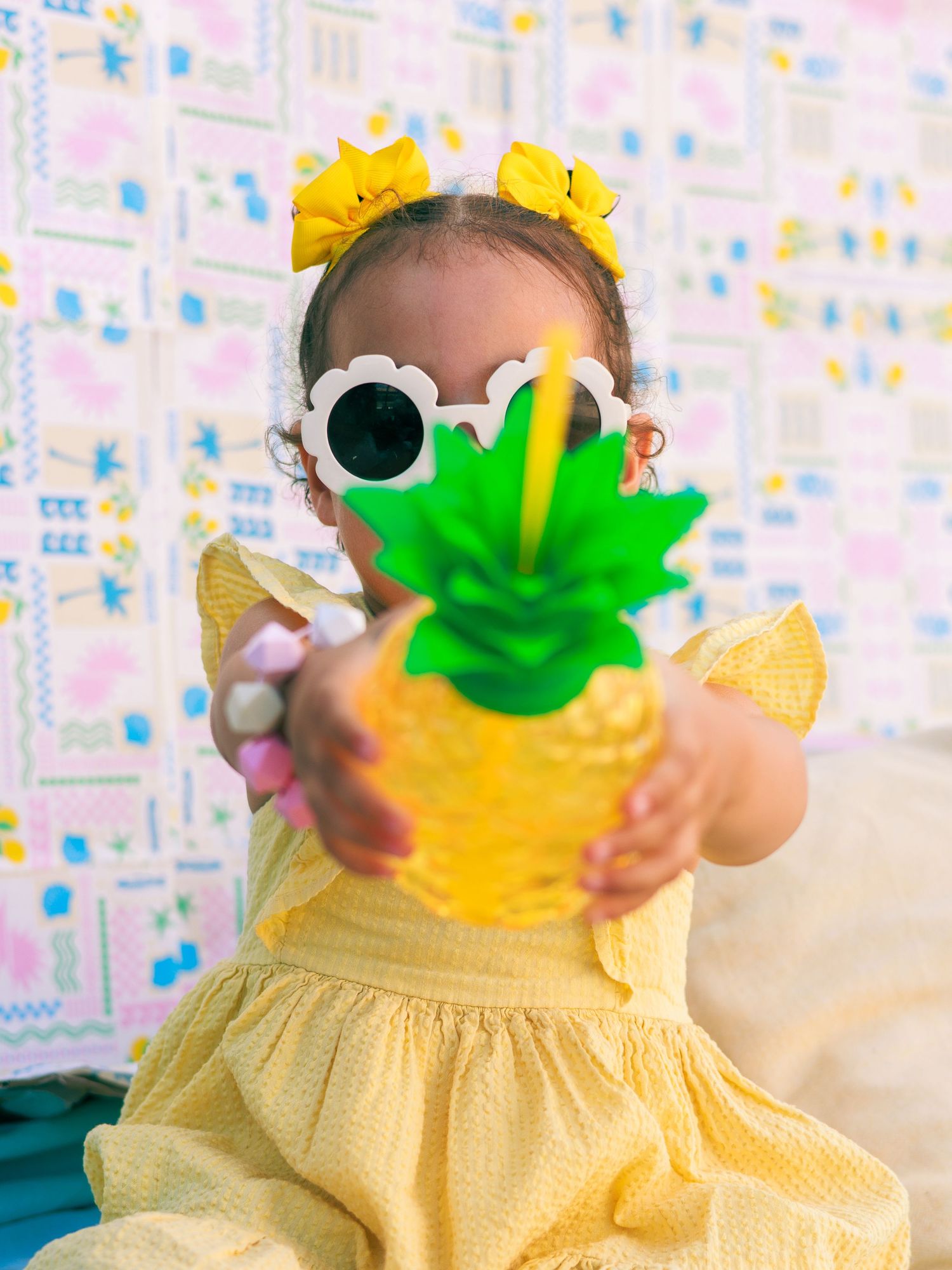 Une petite fille tient une décoration en forme d’ananas pendant une séance photo enfant sur le thème de l’été.