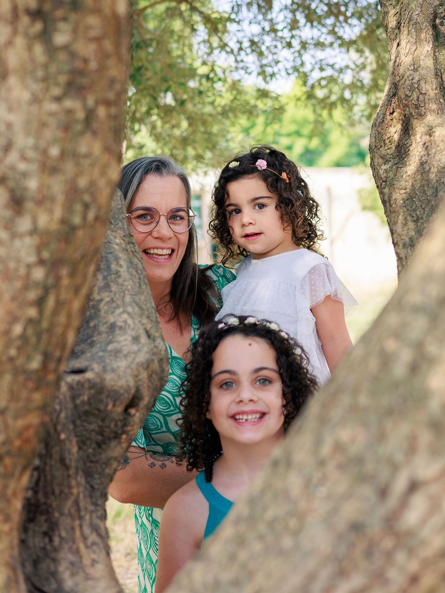 Une maman pose avec ses deux filles entre les arbres pendant une séance photo famille en extérieur.