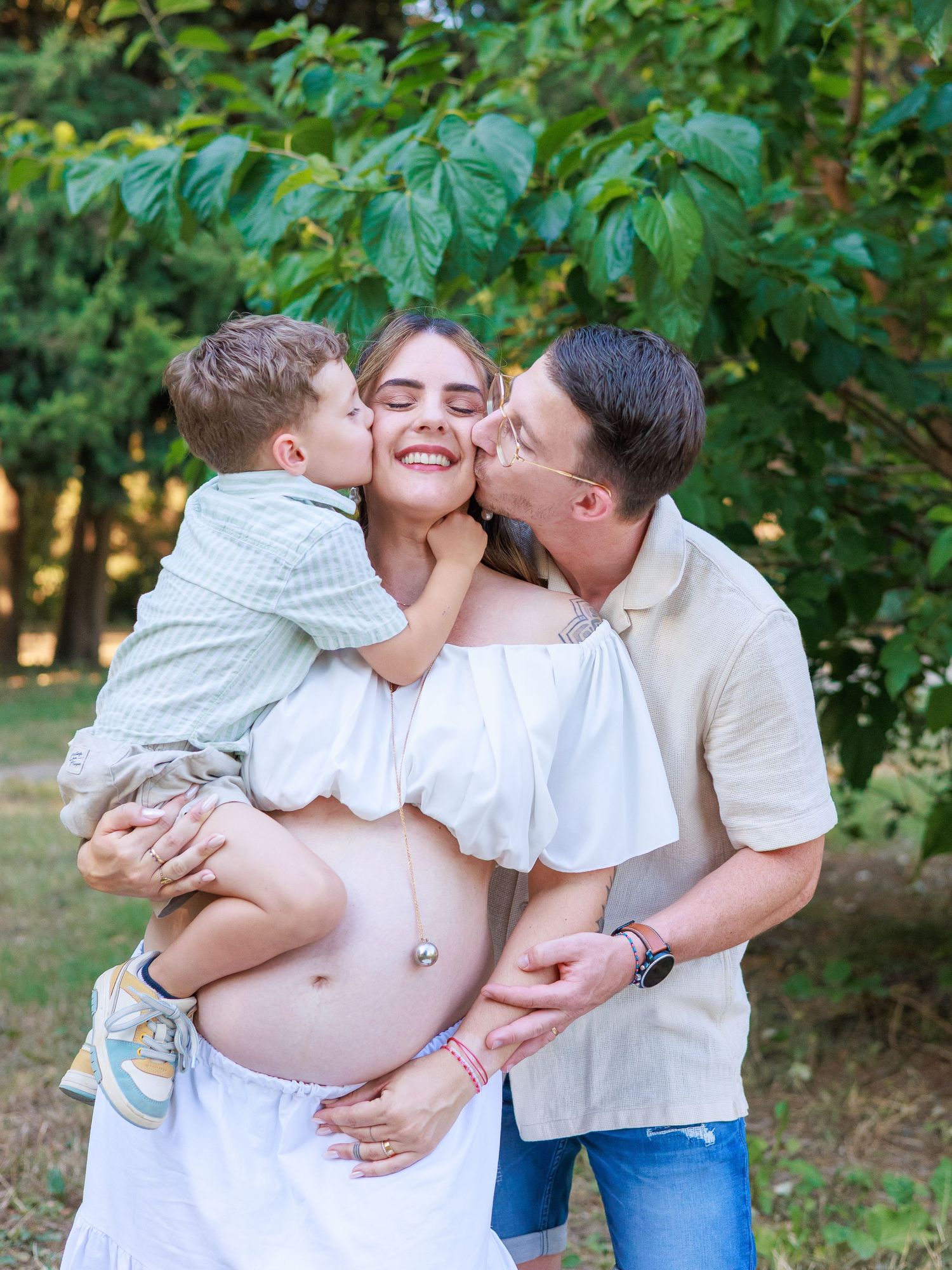 Une famille pose ensemble pendant une séance photo grossesse en extérieur, avec les parents et leur enfant.