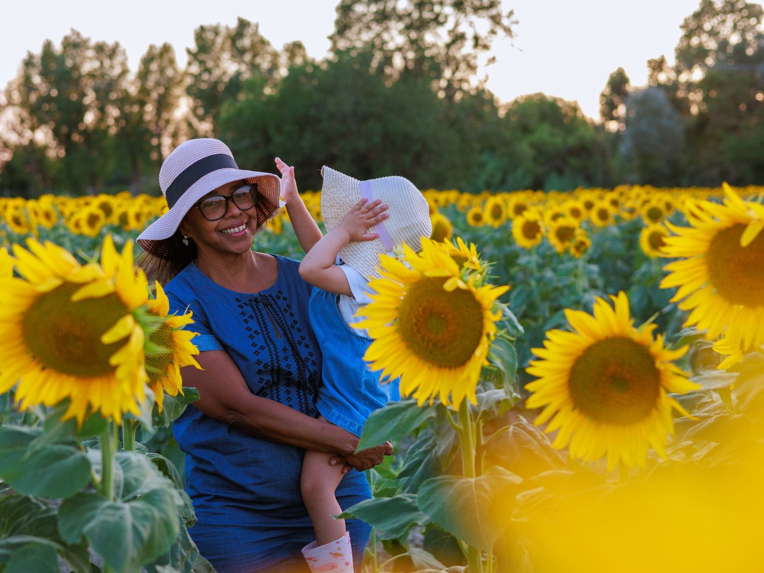 Une maman porte son enfant dans un champ de tournesols pendant une séance photo famille en extérieur.