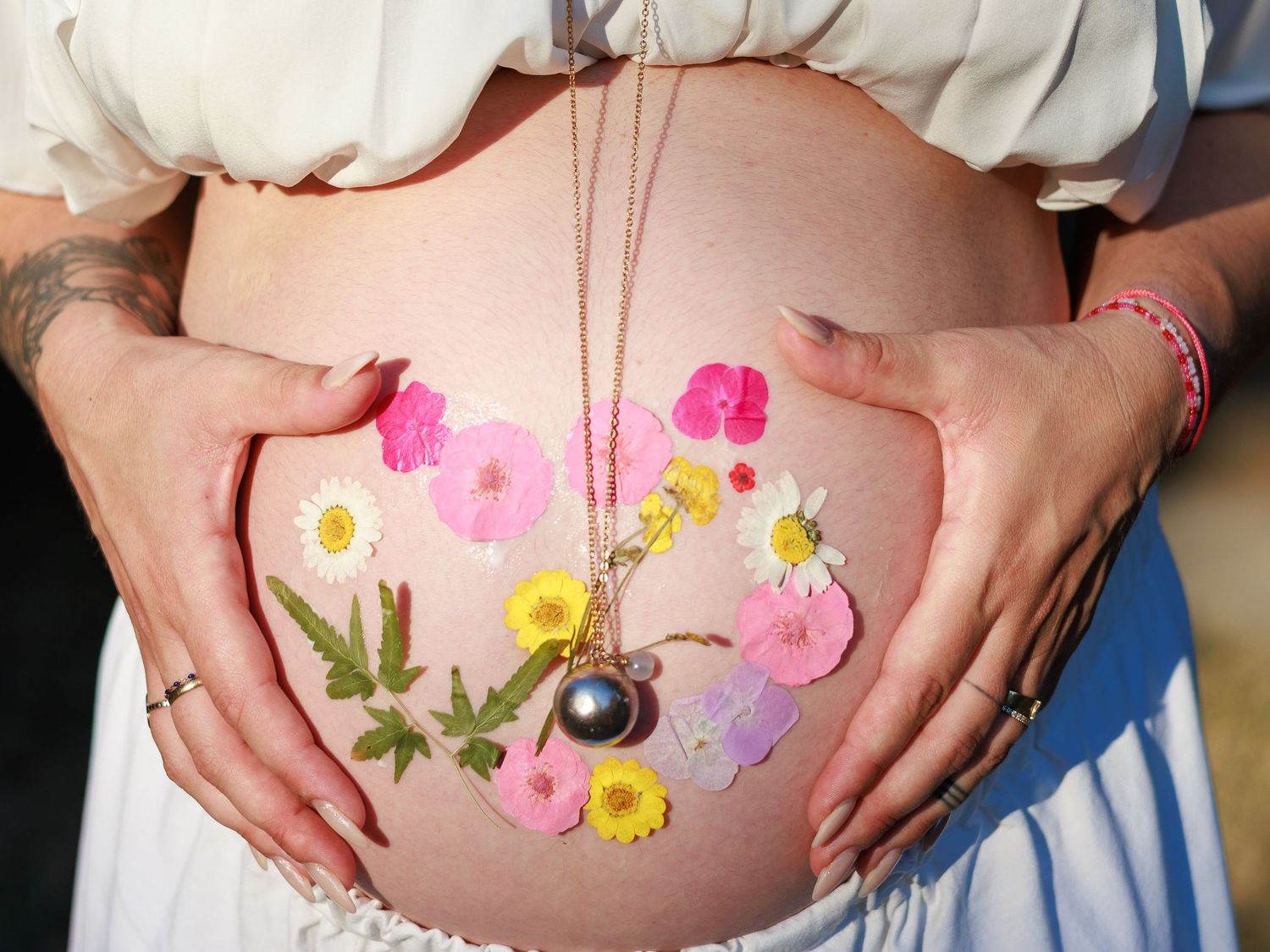 Une future maman tient son ventre décoré de fleurs pendant une séance photo grossesse en extérieur a Avignon