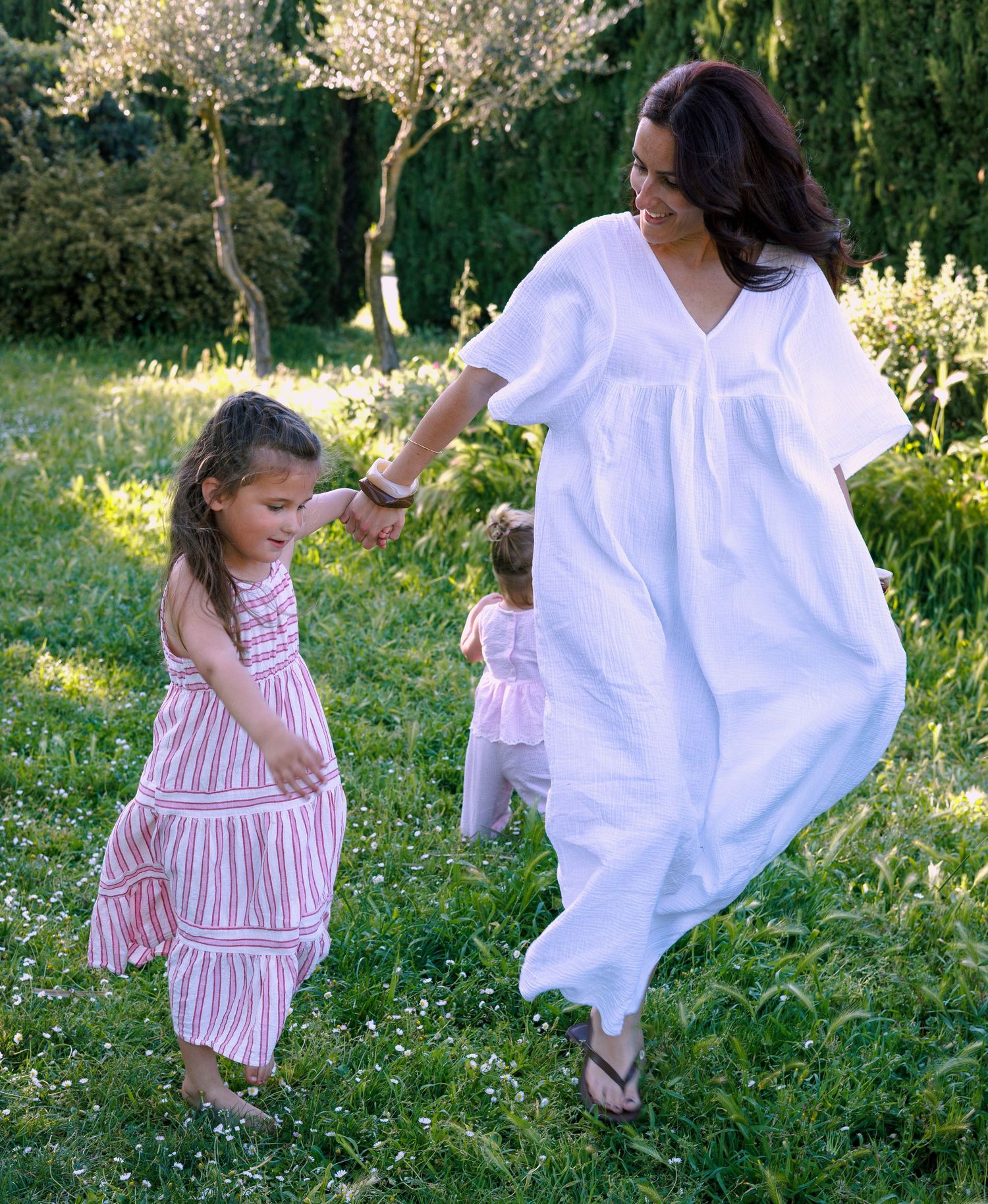 Une maman cour et joue avec ses deux petites filles pendant une séance photo famille en extérieur.