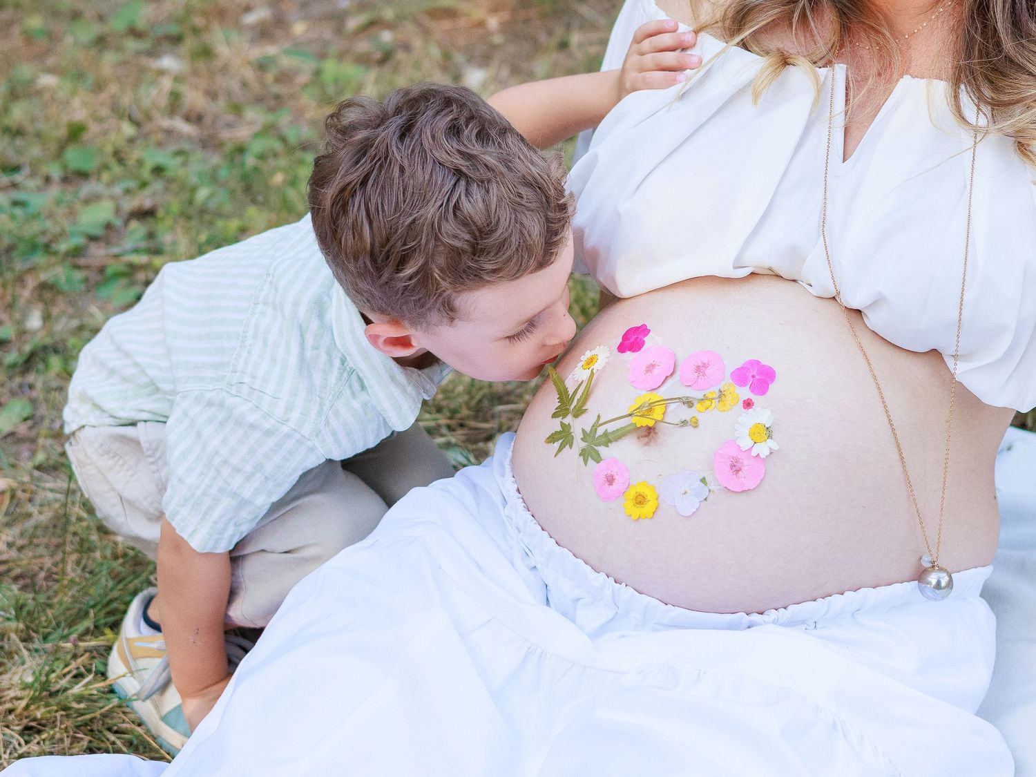 Un enfant embrasse le ventre fleuri de sa maman pendant une séance photo grossesse.