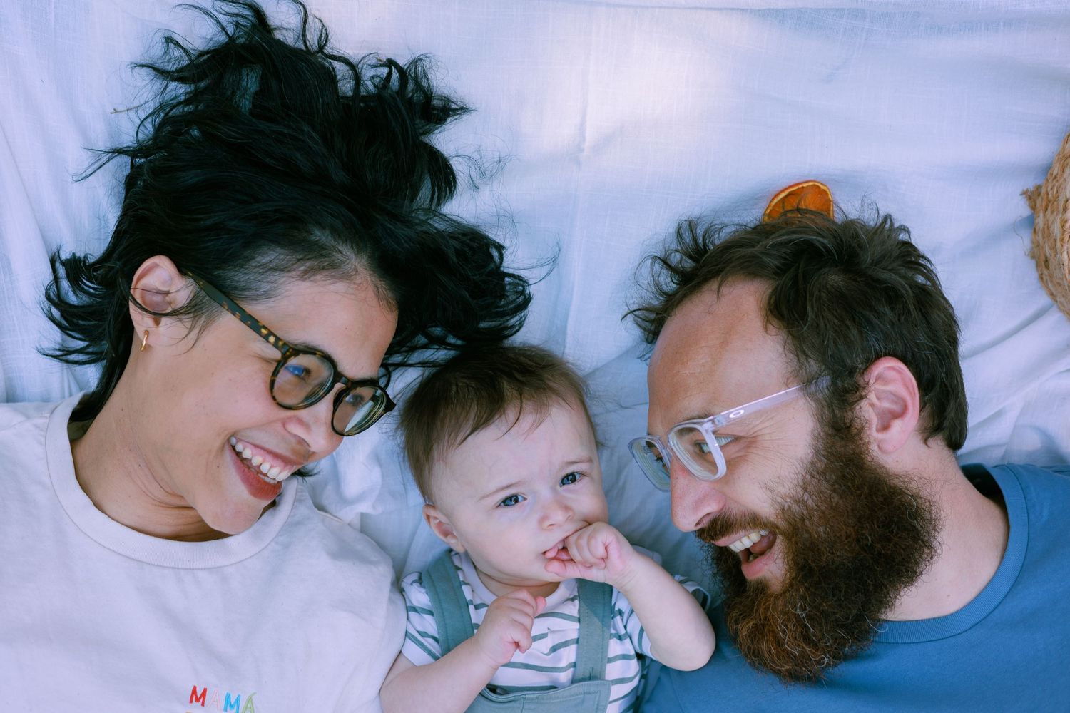 Des parents rient avec leur bébé pendant une séance photo famille en extérieur.